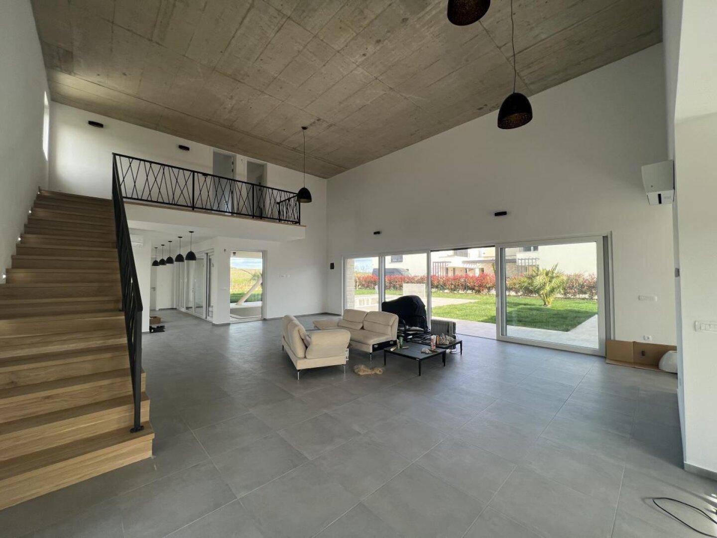 Geräumiger Wohnbereich mit hohen Decken, Sichtbeton und offener Treppe zur Galerie.