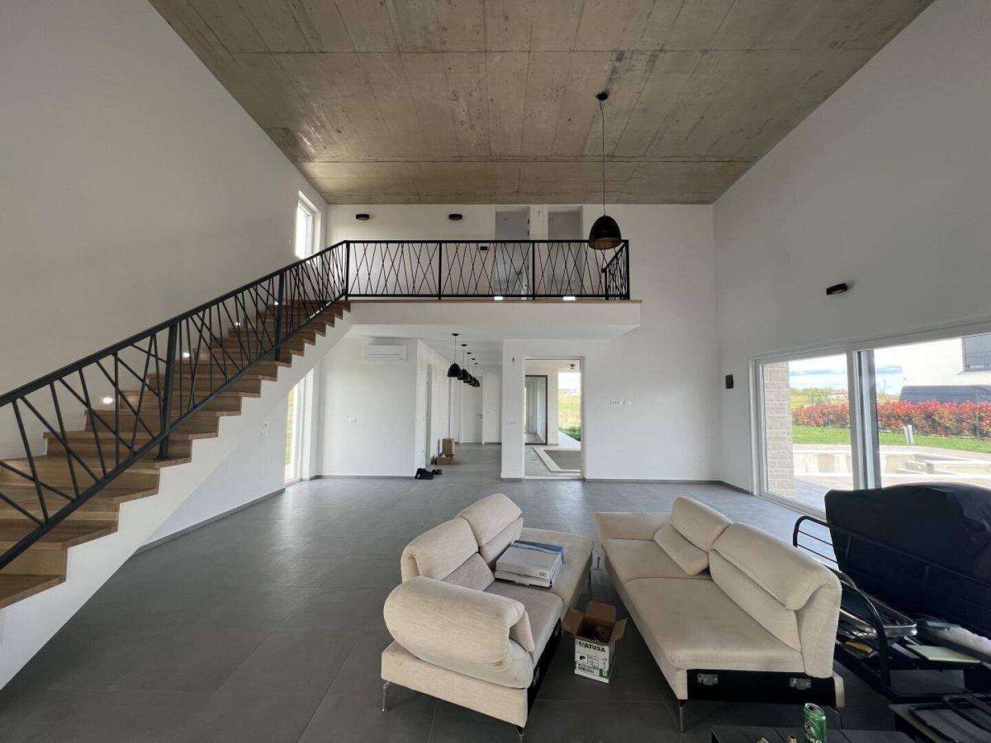 Großzügiger Wohnbereich mit hohen Decken, Sichtbeton und offener Treppe zur Galerie.