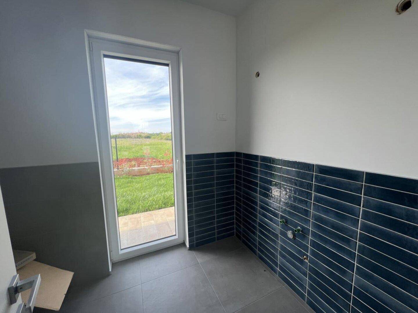 Raum im Bau mit blauen Wandfliesen, Tür zum Garten und Anschlüssen.