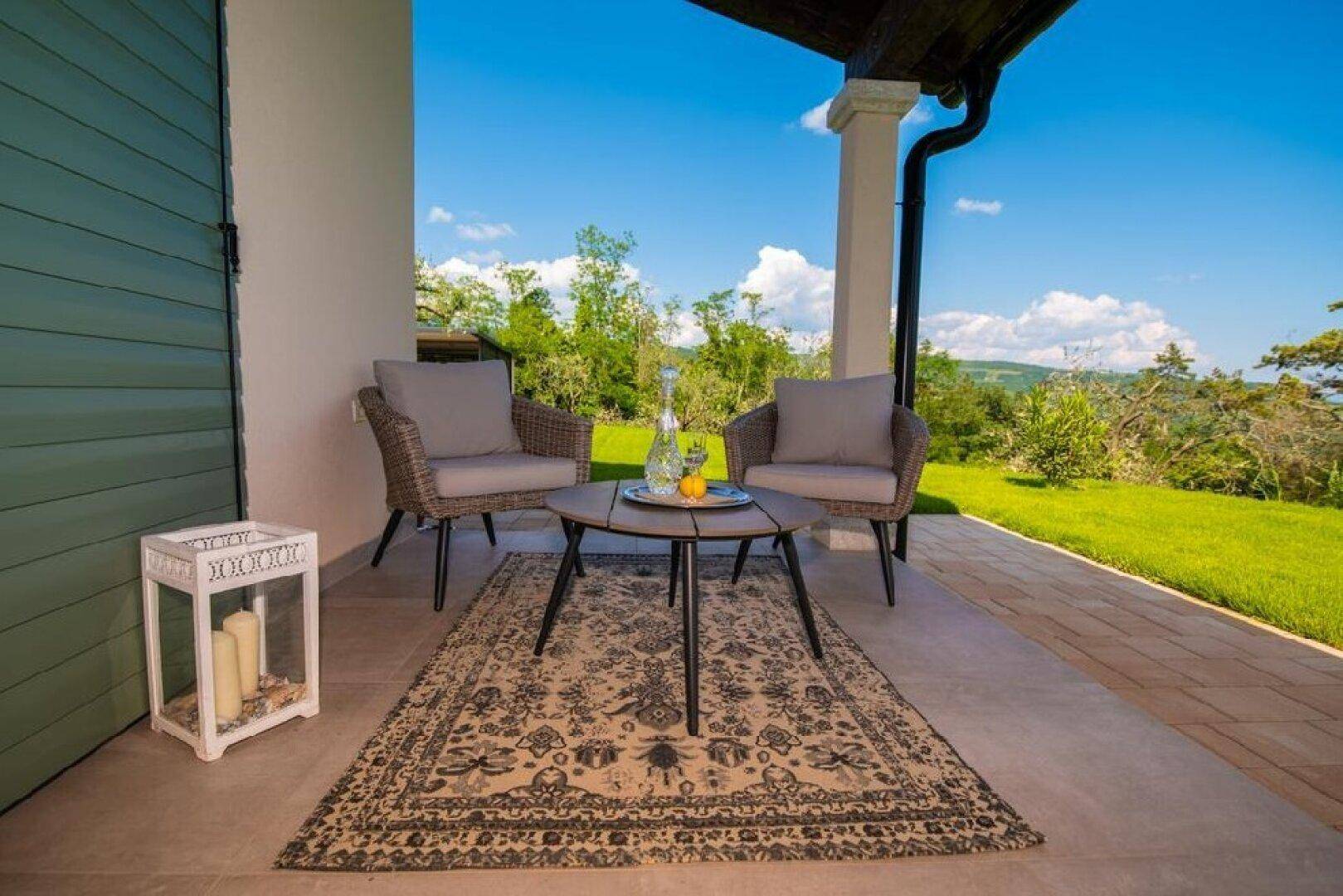 Gemütliche Terrasse mit Sitzgelegenheiten, Teppich und weitem Blick ins Grüne.