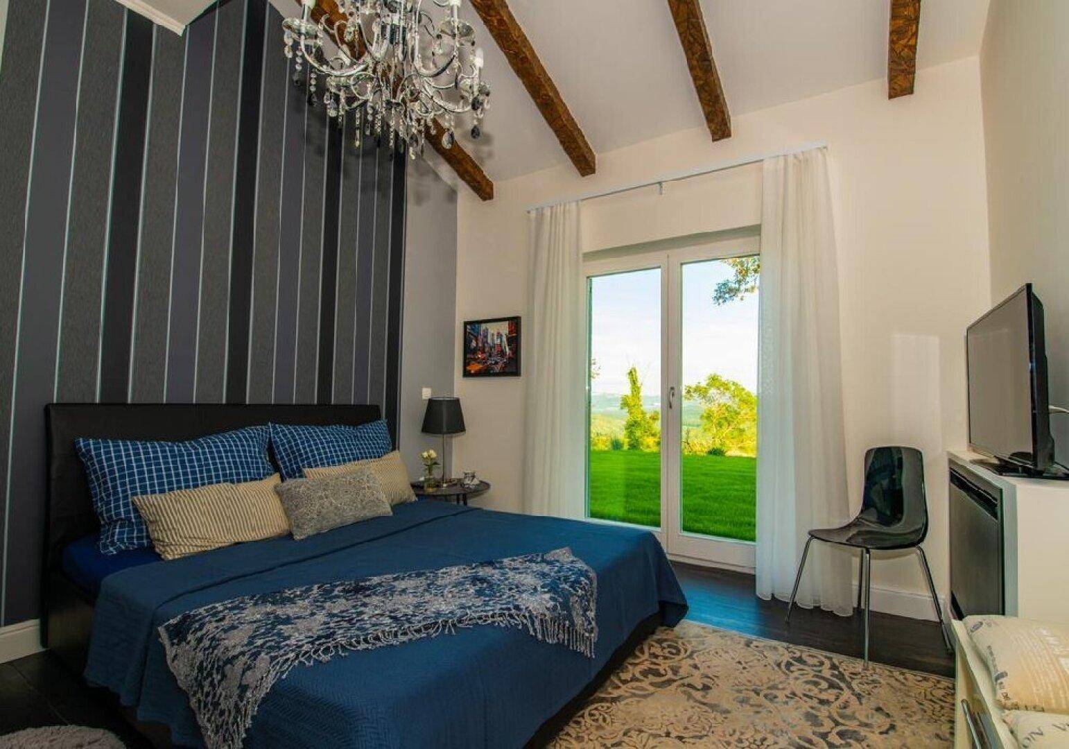 Gemütliches Schlafzimmer mit gestreifter Tapete, Kronleuchter und Zugang zum Garten.