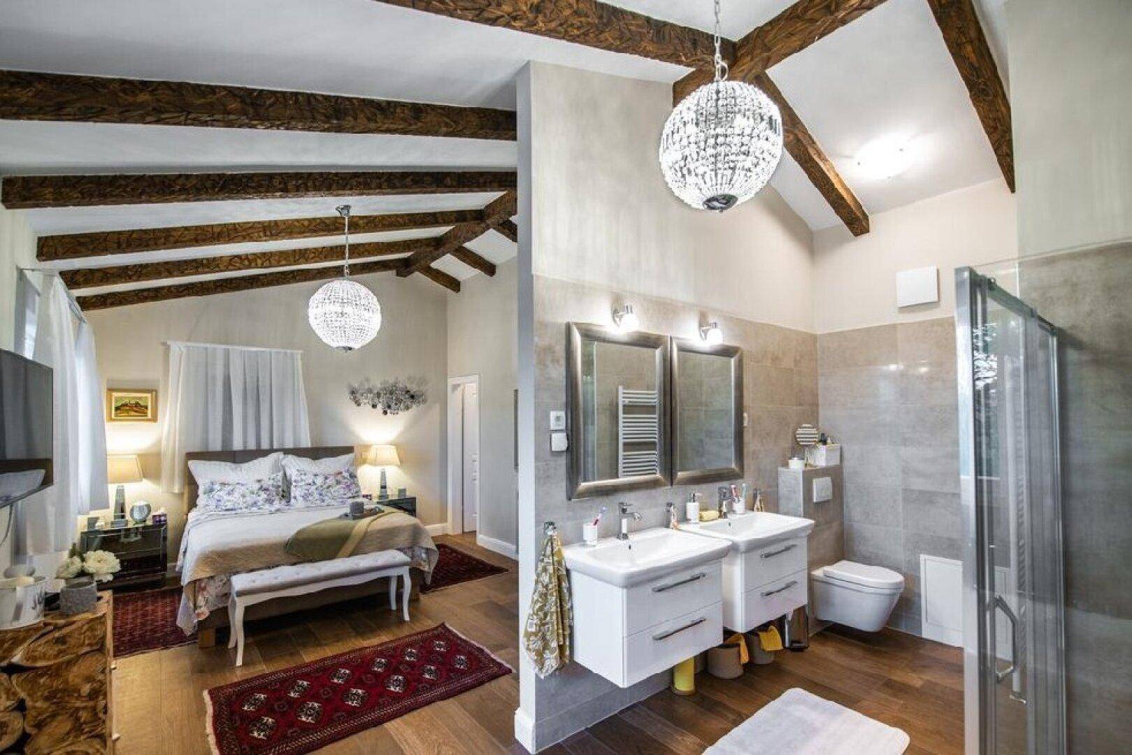 Geräumiges Schlafzimmer mit Holzbalkendecke und offenem Zugang zu einem modernen Badezimmer.