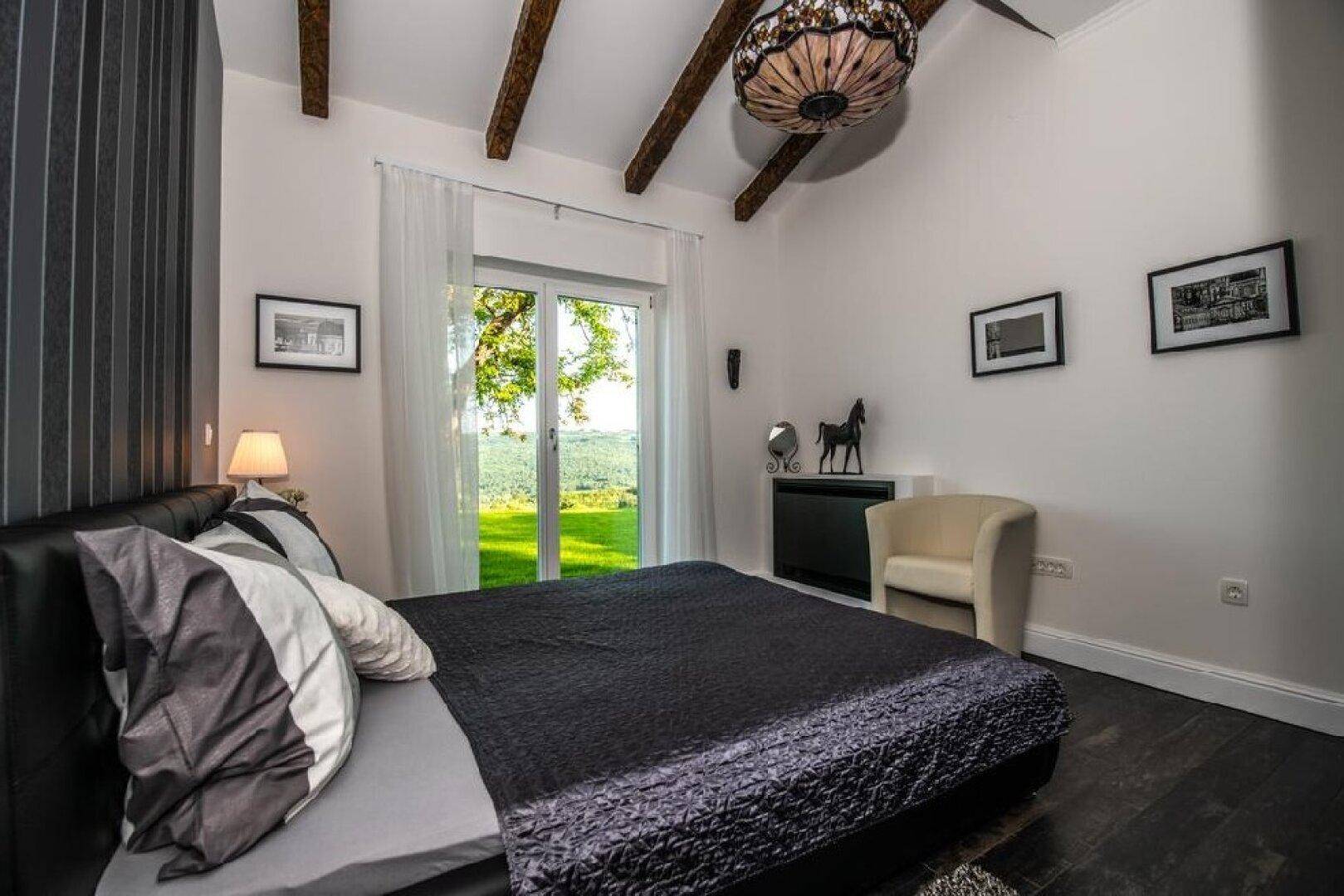 Helles Schlafzimmer mit Holzbalkendecke, dunklem Bett und direktem Zugang zum Garten.