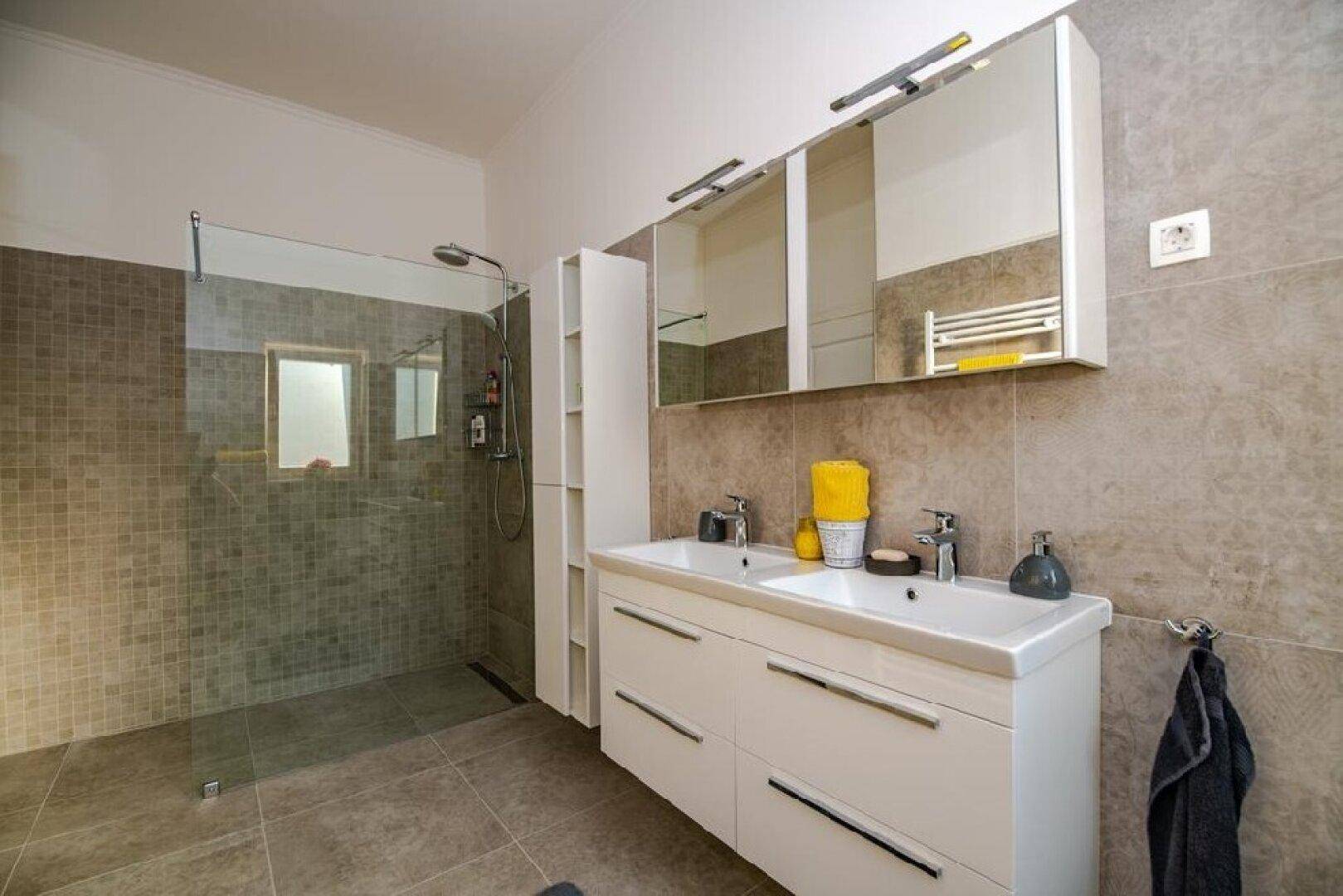 Modernes Badezimmer mit Doppelwaschbecken, großer begehbarer Dusche und grauen Fliesen.