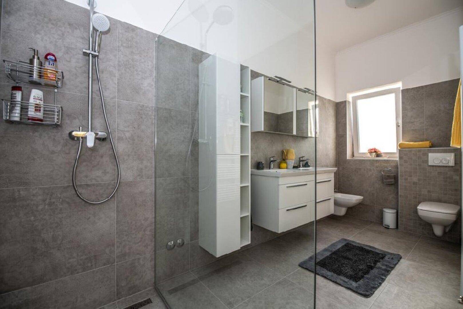 Geräumiges Badezimmer mit begehbarer Dusche, Toilette und Fenster für Tageslicht.