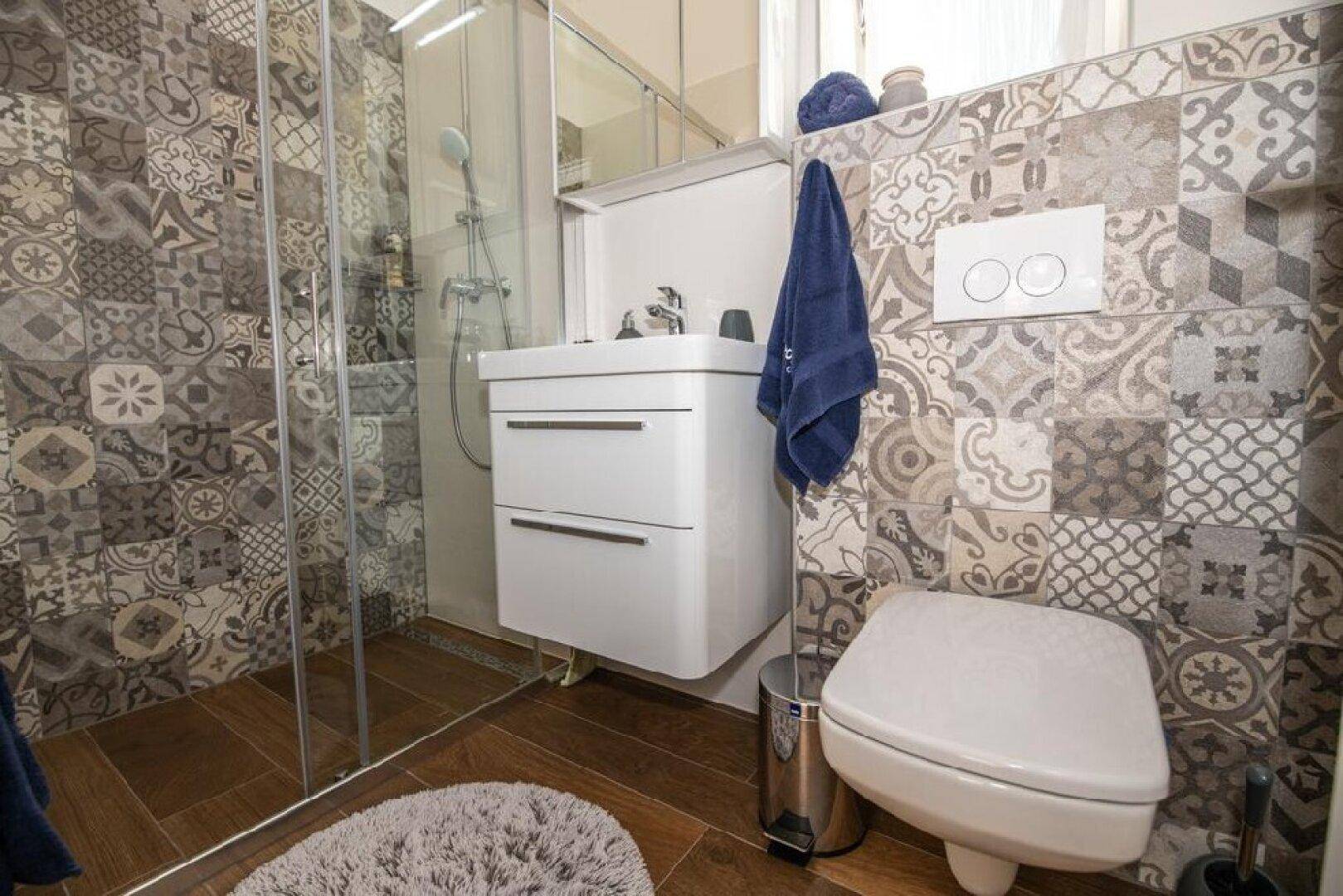 Badezimmer mit gemusterten Fliesen, begehbarer Dusche und modernem Waschbecken.