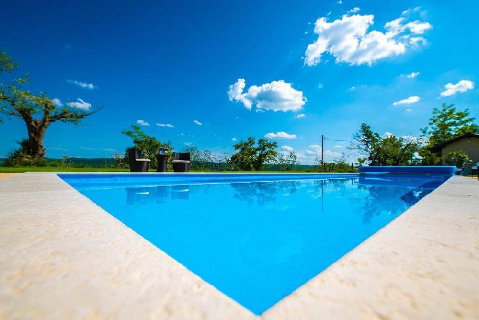 Großer, blauer Swimmingpool unter strahlend blauem Himmel mit grüner Umgebung.