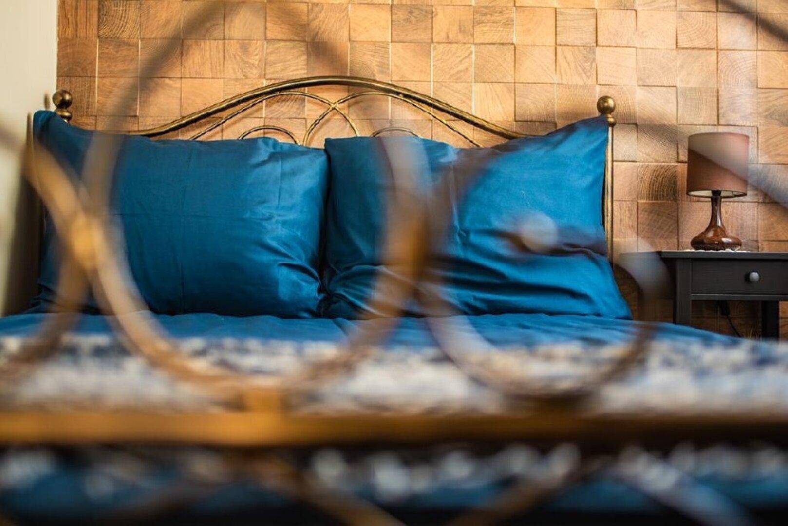 Detailaufnahme eines Bettes mit blauen Kissen und dekorativer Holzvertäfelung als Kopfteil.