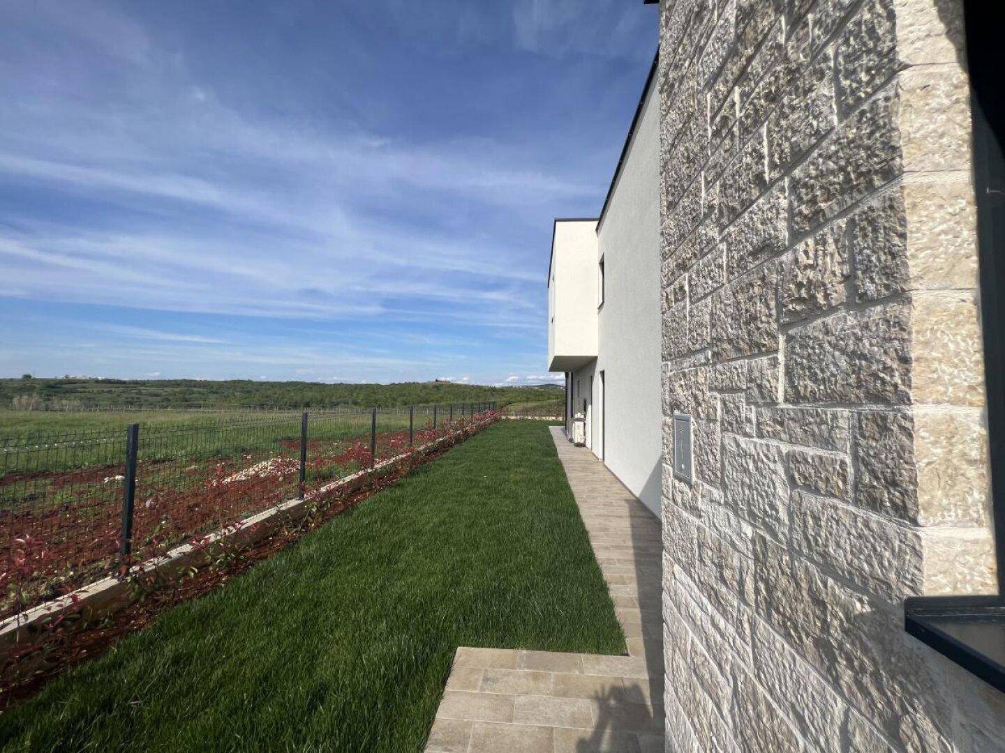 Seitenfassade der Villa mit Natursteinverkleidung und Blick auf die weite Landschaft.