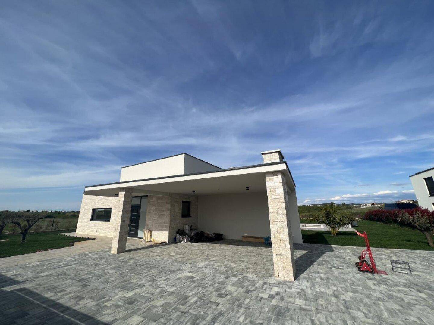 Eingangsbereich der modernen Villa mit überdachtem Carport und gepflasterter Auffahrt.