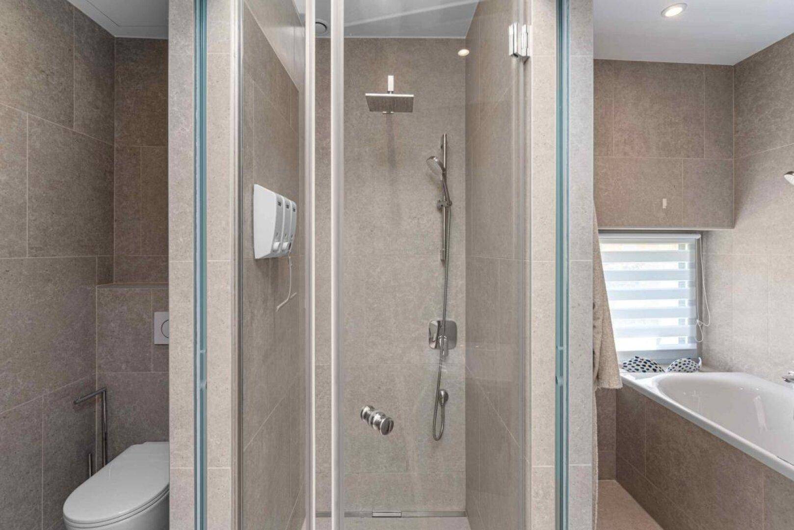 Modernes Badezimmer mit begehbarer Dusche, Badewanne und Wand-WC, komplett gefliest.