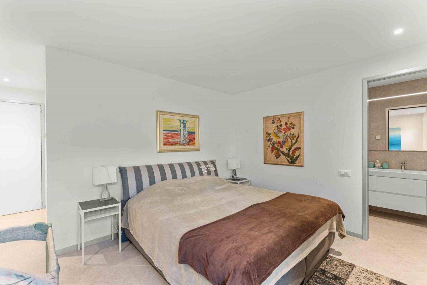 Komfortables Schlafzimmer mit Doppelbett und Kunstwerken, angrenzend an ein modernes Bad.