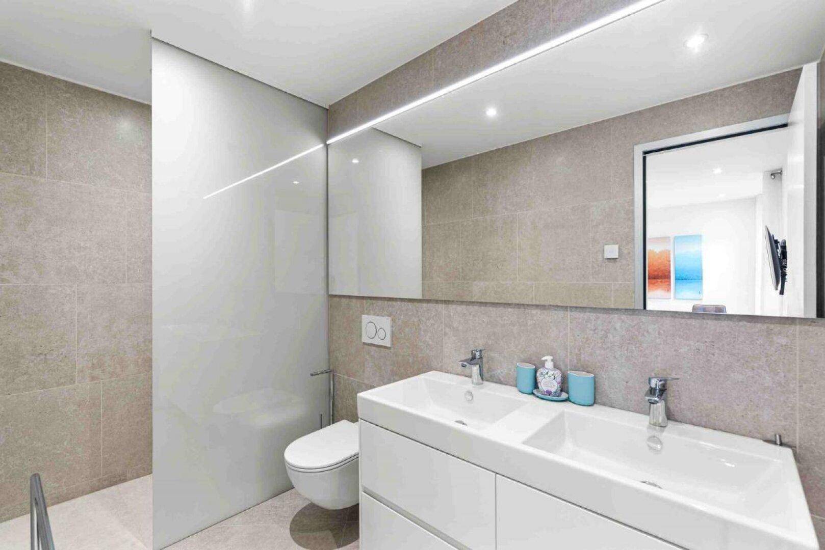 Modernes Badezimmer mit Doppelwaschbecken, großem Spiegel und separatem WC-Bereich.