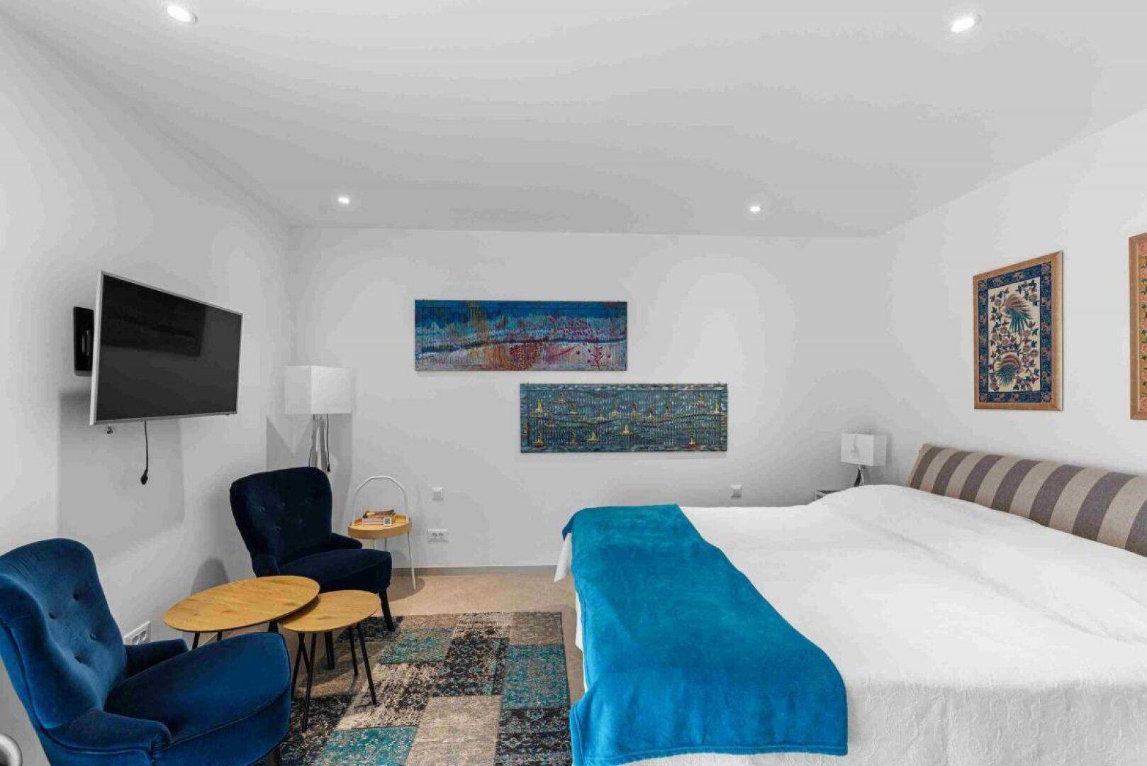 Helles Schlafzimmer mit Doppelbett, zwei bequemen Sesseln und Wandfernseher.