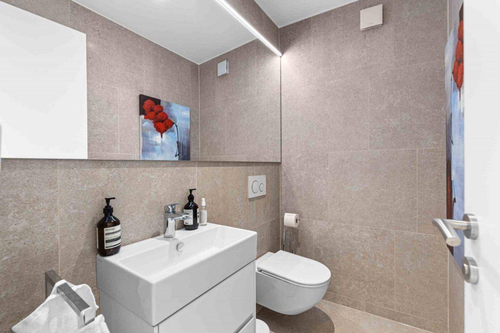 Modernes Gäste-WC mit Einzelwaschbecken und Wand-WC, komplett gefliest.