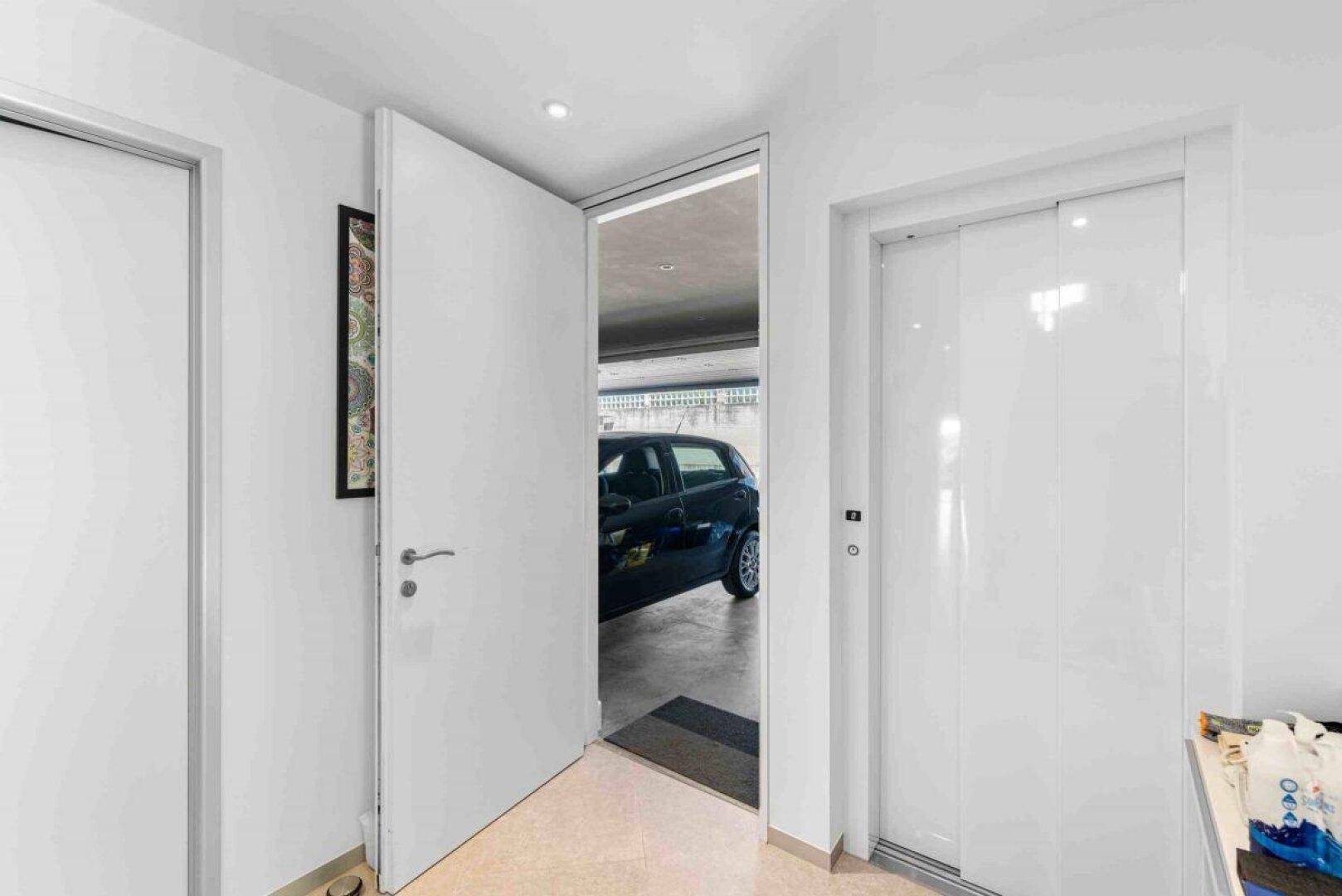 Heller Flur mit Zugang zur Garage und einem modernen Aufzug im Hintergrund.