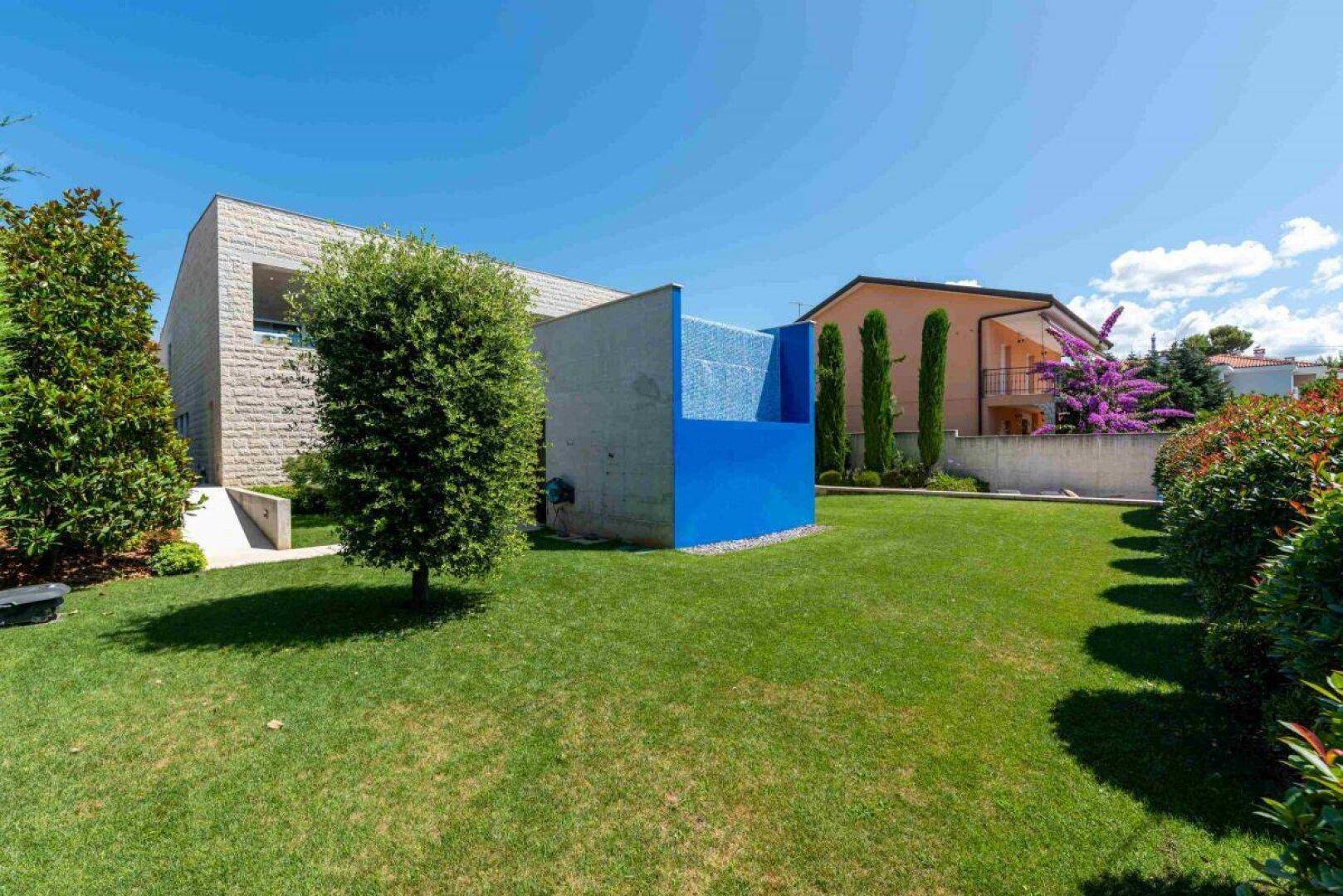 Moderne Architektur mit weitläufigem Rasen und markanter blauer Wand im Gartenbereich.