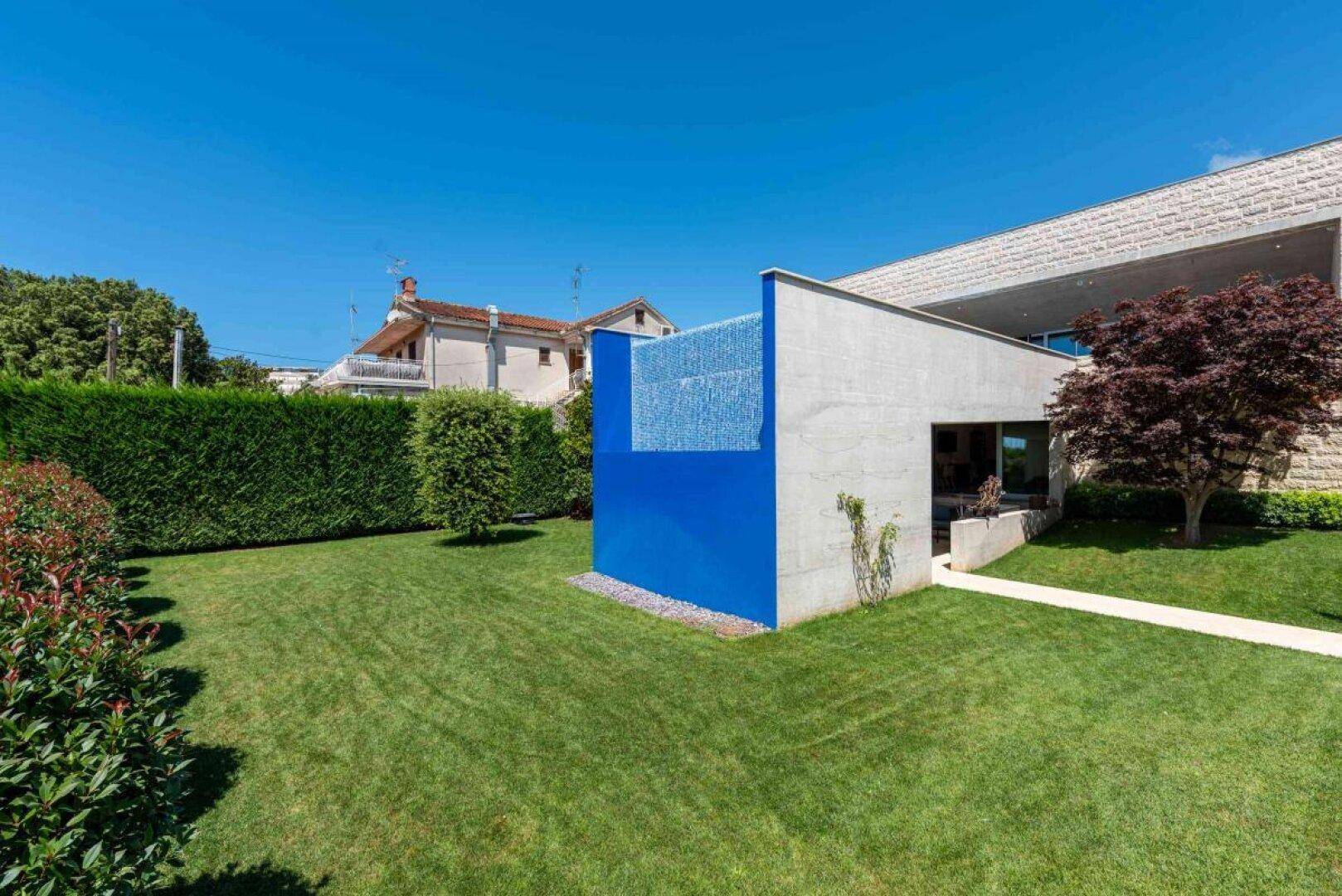 Weitläufiger Gartenbereich mit modernem Haus, blauer Wand und gepflegten Hecken.
