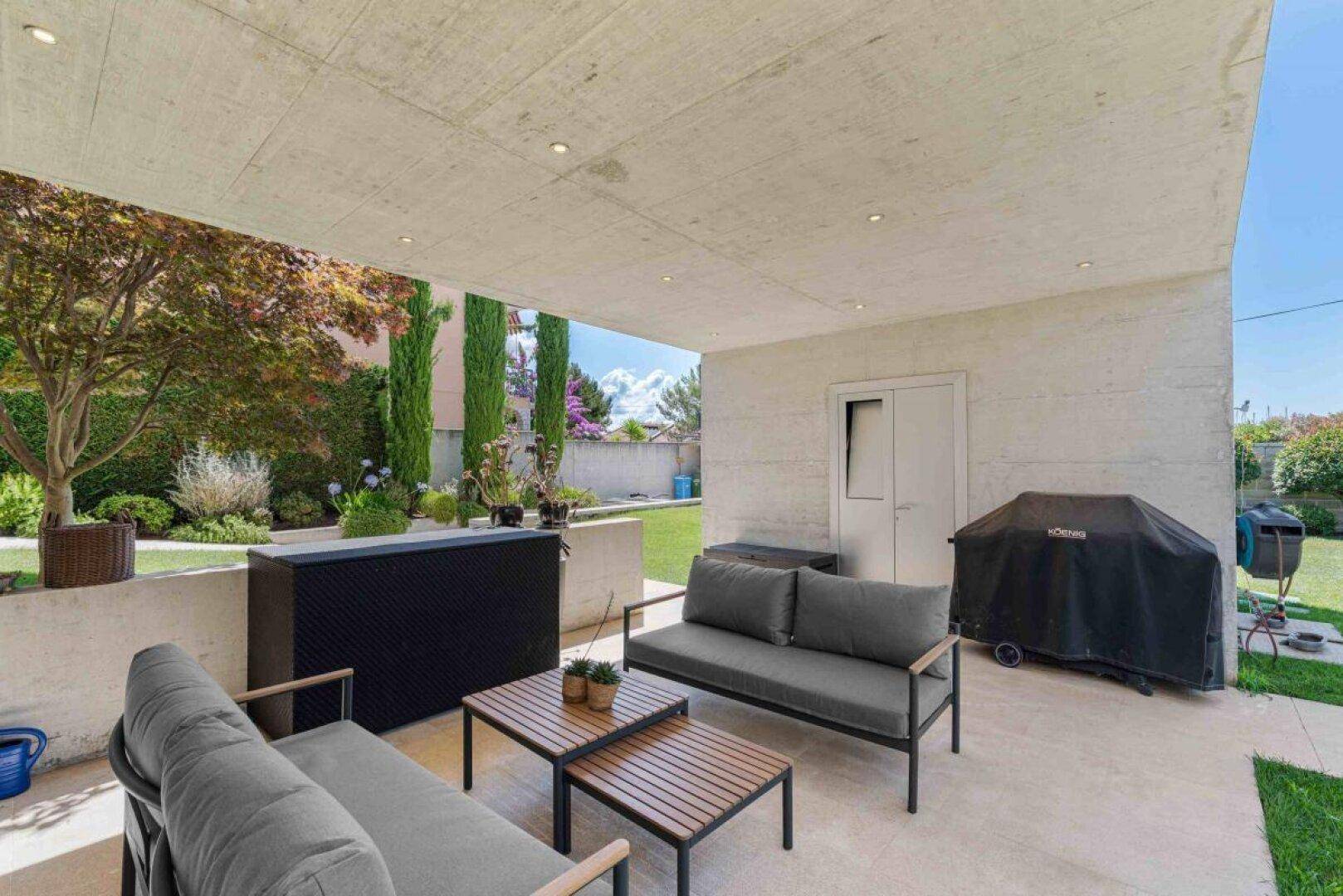 Überdachte Terrasse mit modernen Gartenmöbeln, Grillbereich und Blick ins Grüne.