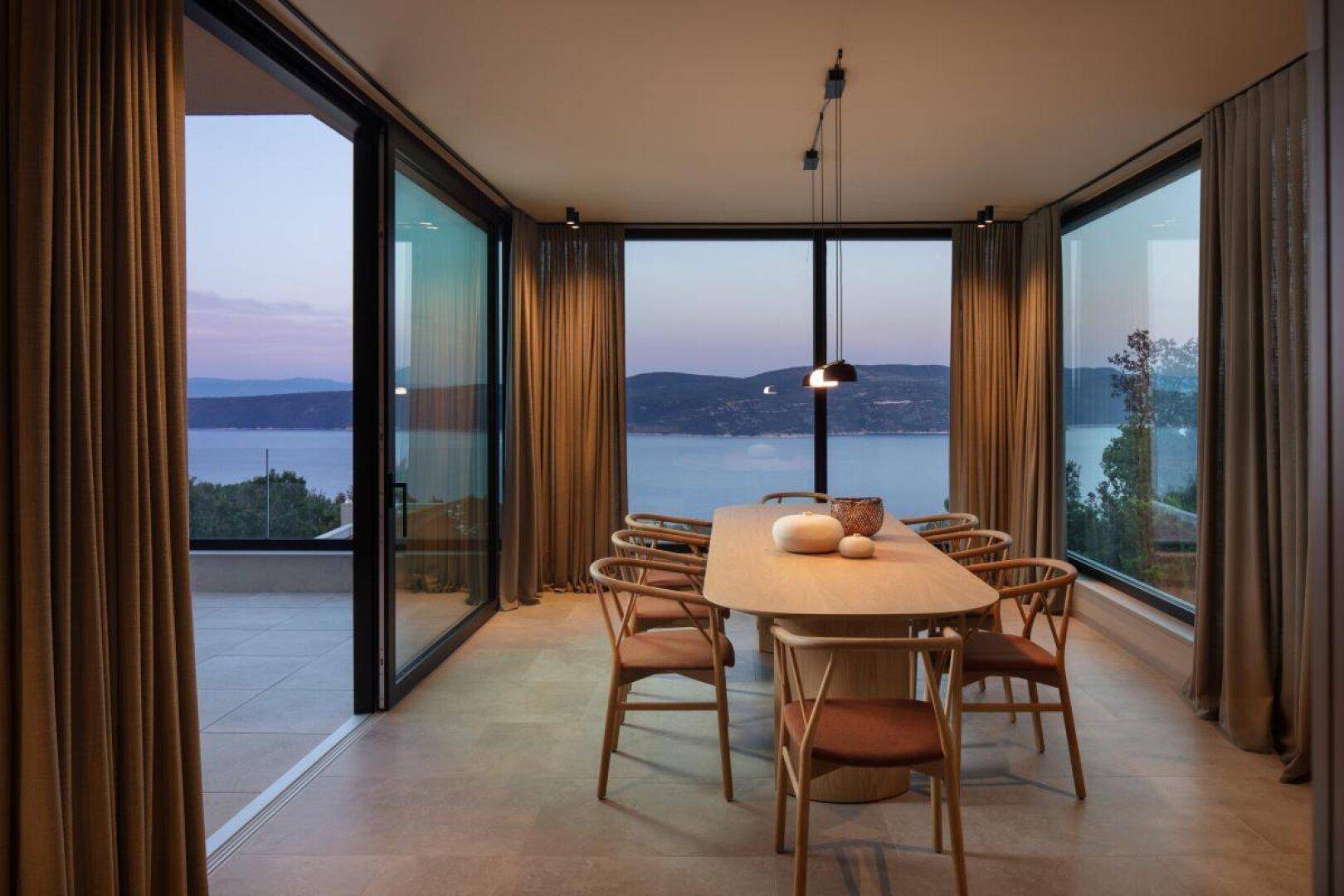 Moderner Essbereich mit Holztisch und Stühlen, großen Fenstern und atemberaubendem Meerblick.