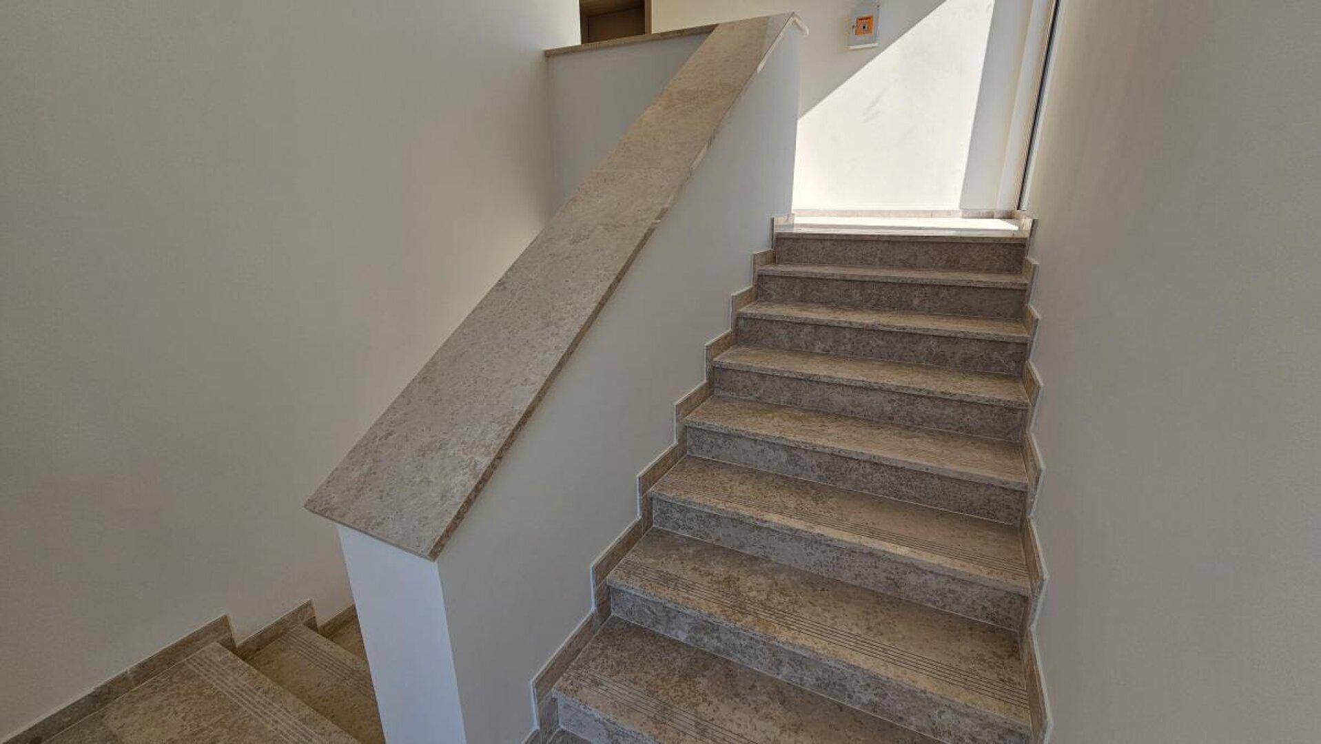 Treppenhaus mit Steinstufen und schlichter Brüstung, verbindet die verschiedenen Ebenen des Hauses.