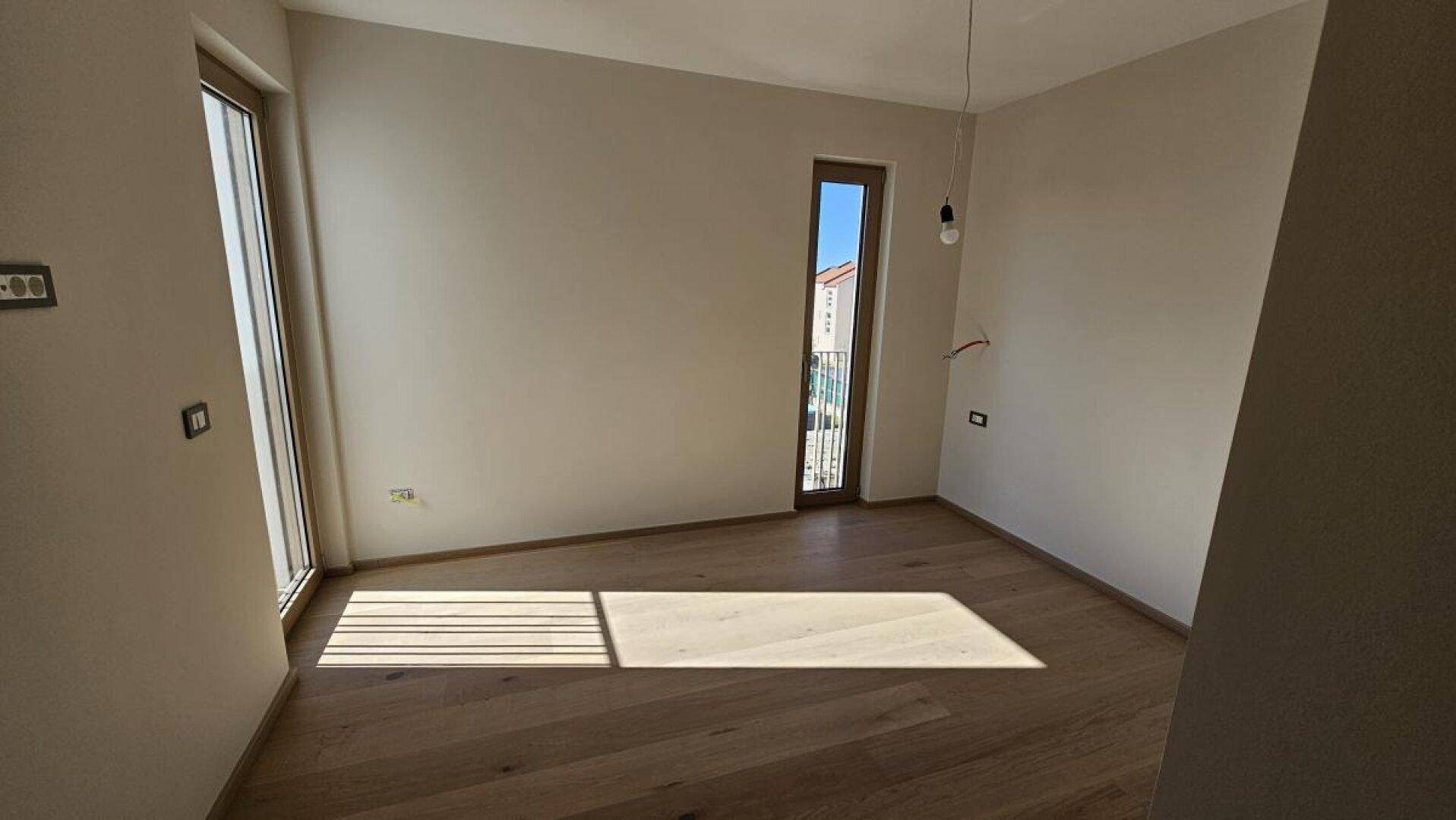 Helles Schlafzimmer mit zwei Fenstern und Holzboden, bietet viel Tageslicht und eine angenehme Atmosphäre.