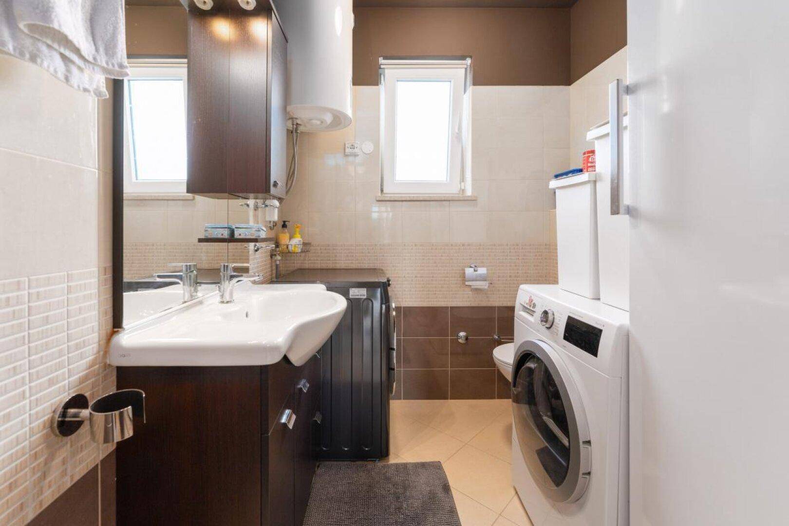 Badezimmer mit Waschbecken, Toilette und integrierter Waschmaschine.
