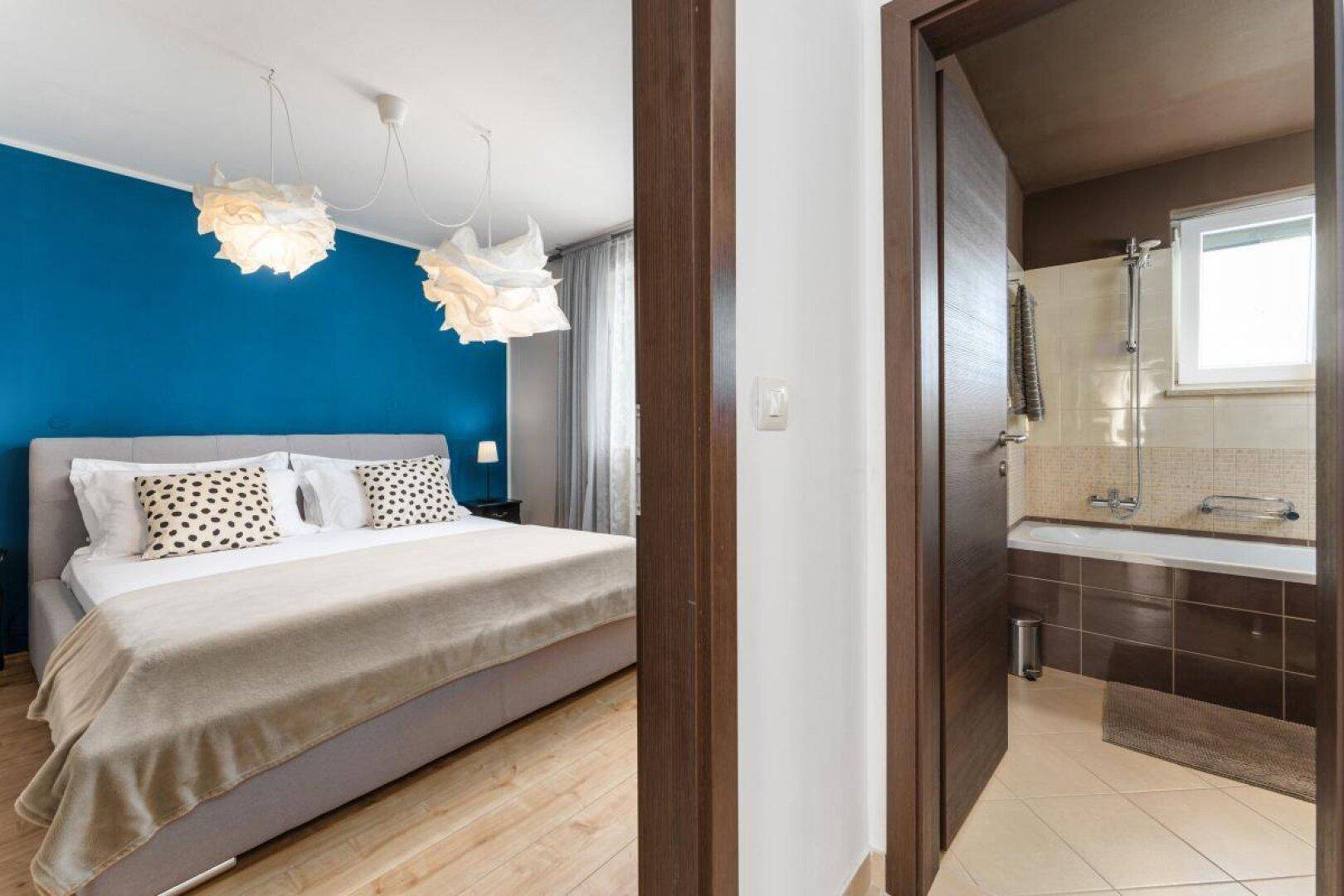 Schlafzimmer mit blauer Akzentwand, Doppelbett und direktem Zugang zum Badezimmer.