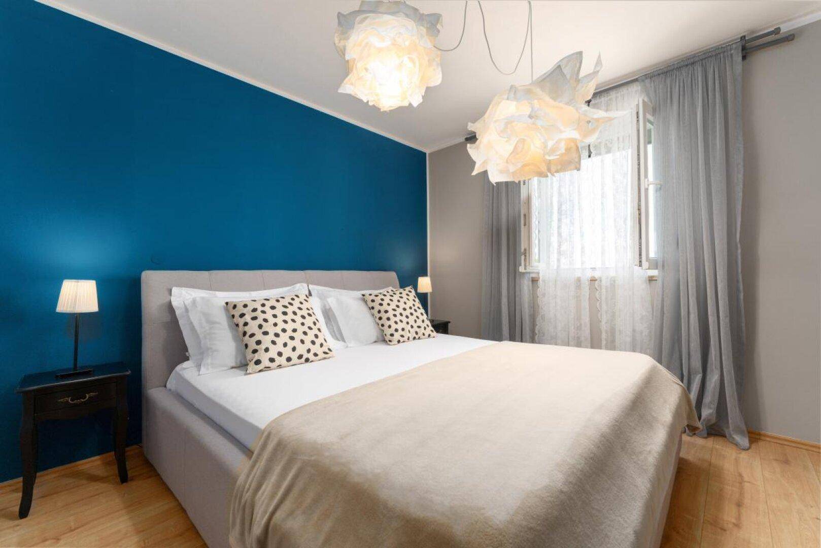 Helles Schlafzimmer mit modernem Bett, blauer Akzentwand und dekorativen Leuchten.