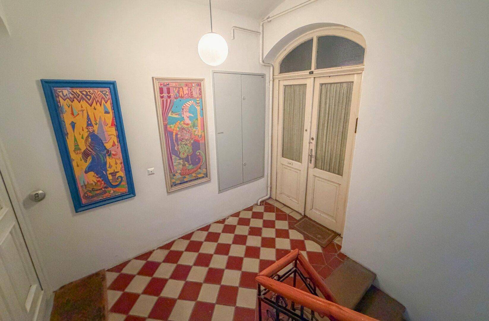 Heller Eingangsbereich mit Schachbrettmuster-Fliesenboden und dekorativen Bildern an der Wand.