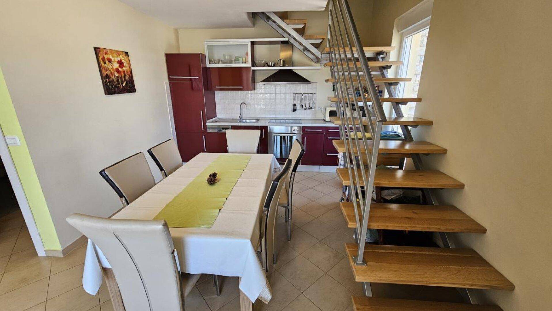 Essbereich mit großem Tisch, angrenzender Küche und moderner offener Holztreppe.