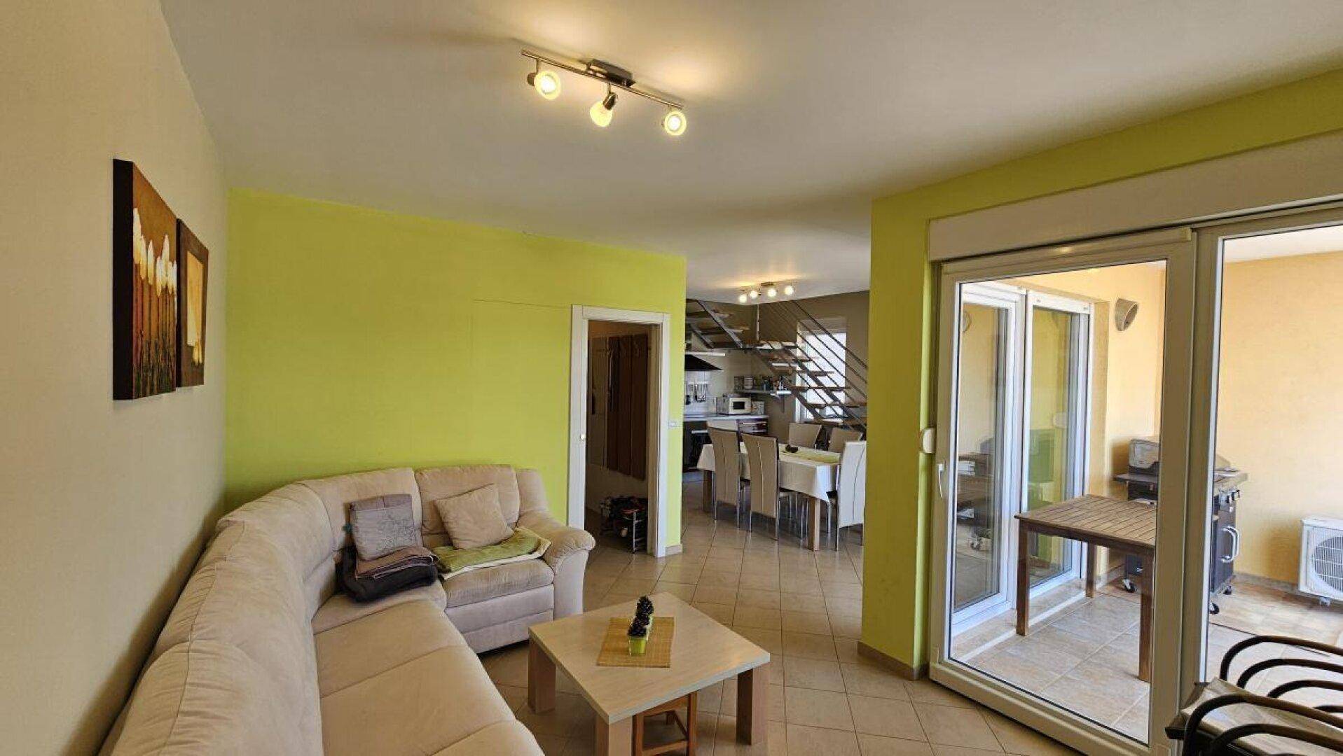 Gemütliches Wohnzimmer mit Sofa, hellgrünen Wänden und Zugang zu einem Balkon.
