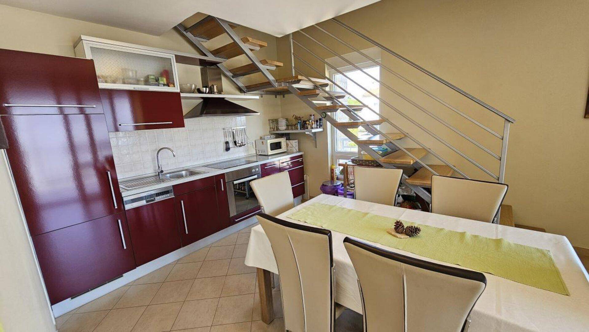 Moderne Küche mit roten Schränken, Essbereich und offener Holztreppe zum Obergeschoss.