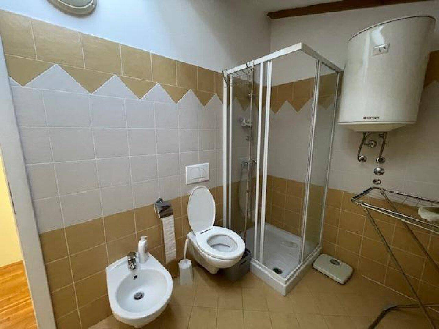 Badezimmer mit Duschkabine, Toilette, Bidet und Fliesen an Wänden und Boden.
