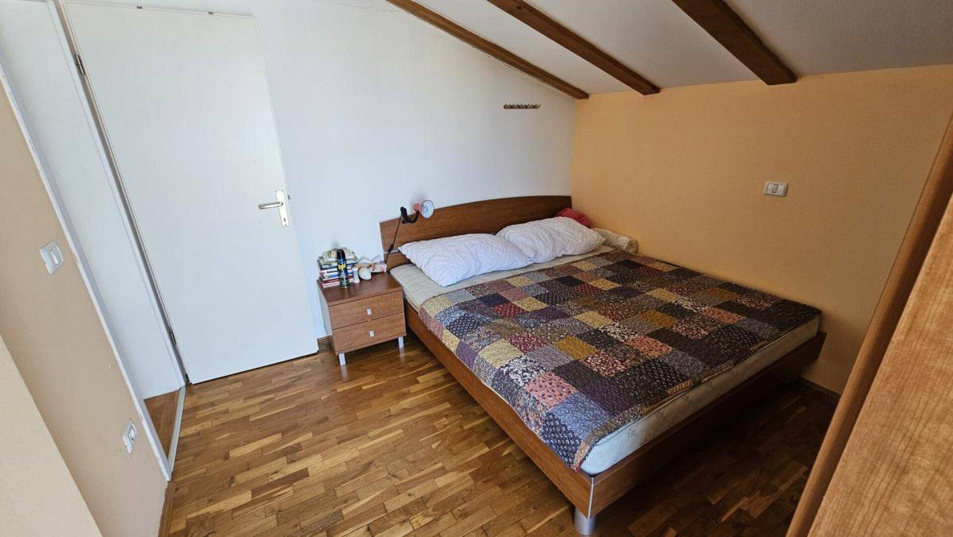 Schlafzimmer im Dachgeschoss mit Doppelbett, Holzboden und sichtbaren Deckenbalken.