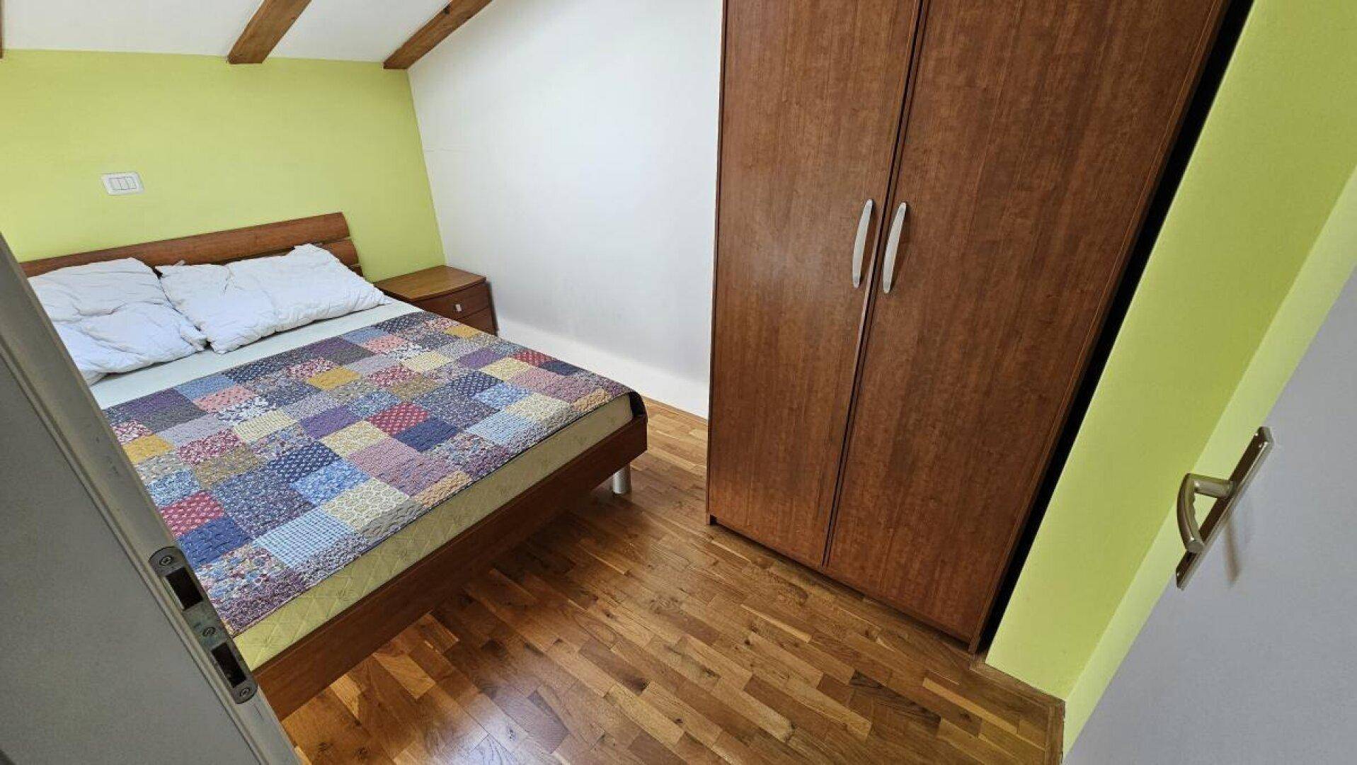 Gemütliches Schlafzimmer mit Holzboden, Kleiderschrank und grüner Akzentwand im Dachgeschoss.