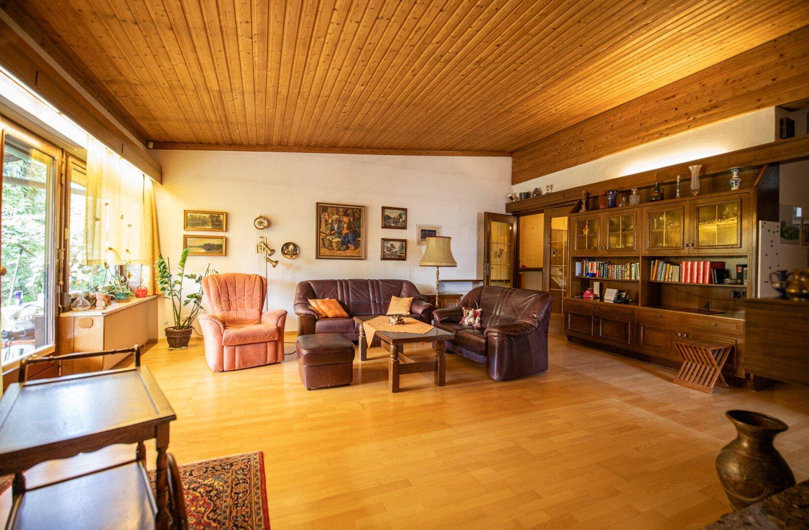 Geräumiges Wohnzimmer mit Holzbalkendecke, Parkettboden und traditioneller Einrichtung, hell durch große Fenster.