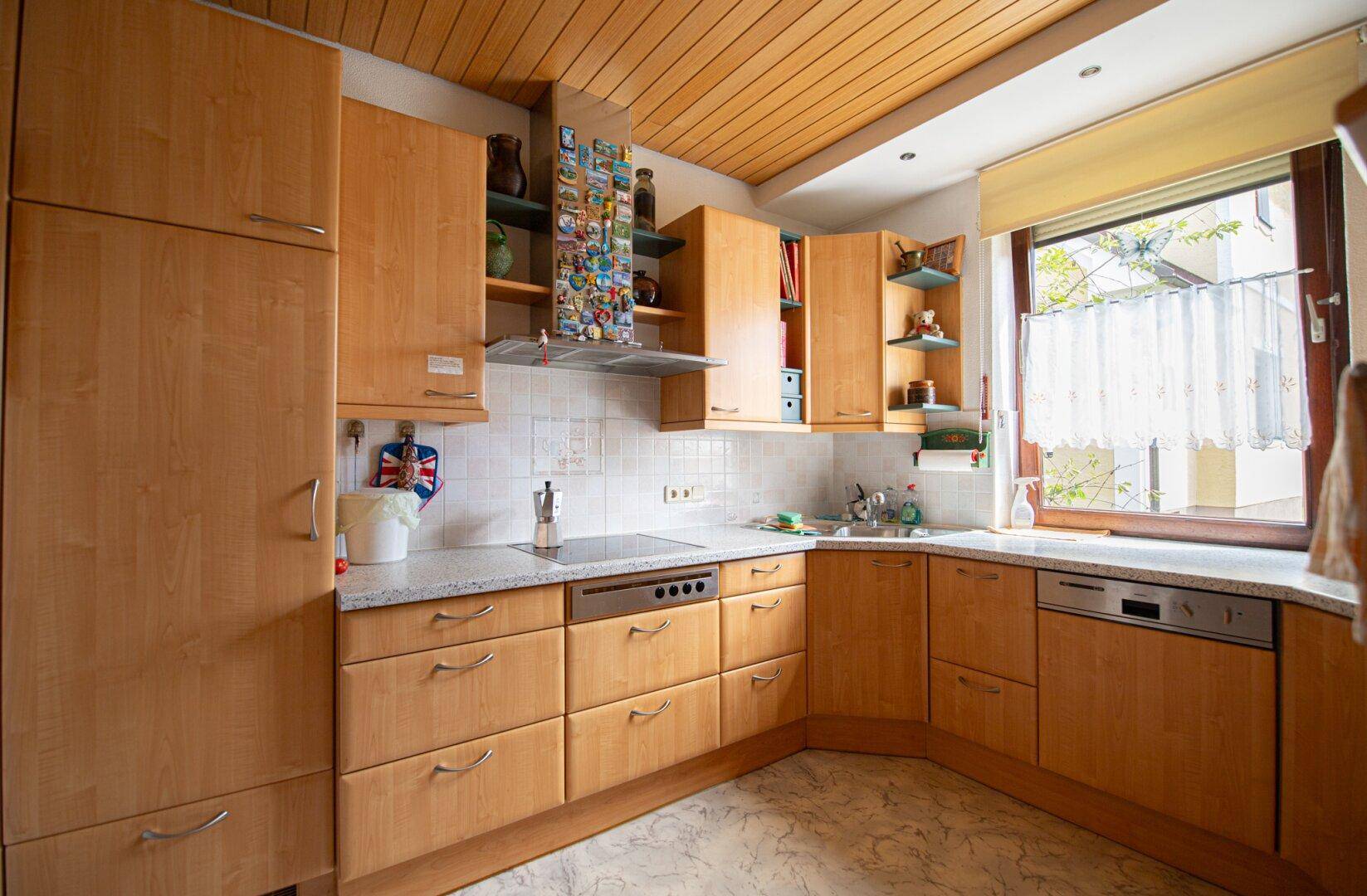 Funktionale Küche mit hellen Holzschränken, Granitarbeitsplatte und Fenster, bietet ausreichend Stauraum.
