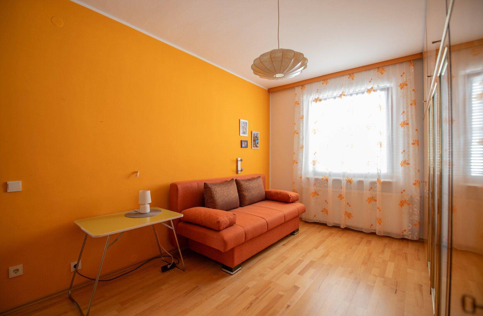 Freundliches Zimmer mit orangefarbener Wand und Holzfußboden, bietet eine gemütliche Atmosphäre.