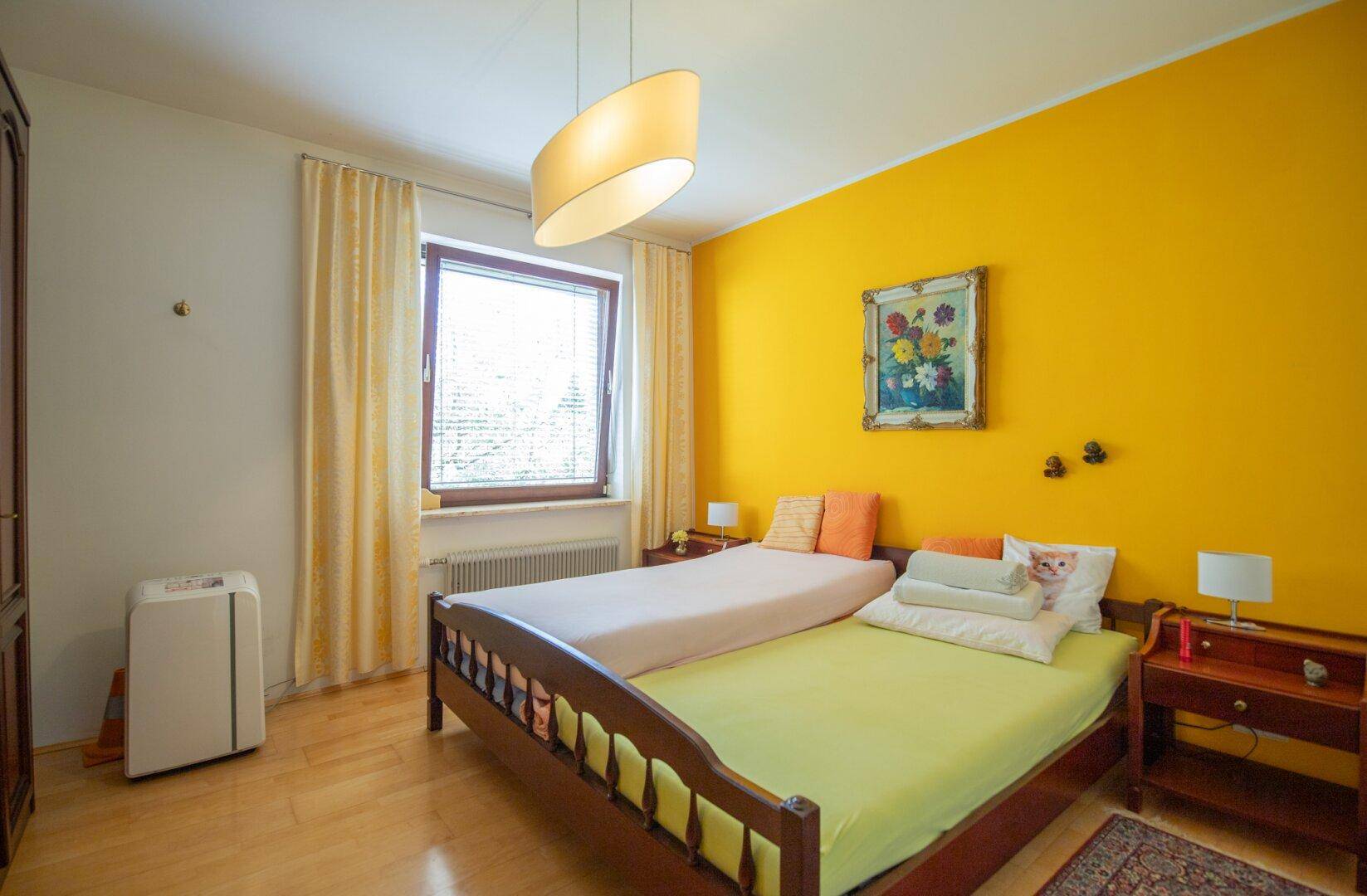 Schlafzimmer mit gelber Akzentwand, zwei Einzelbetten und Holzfußboden, hell und freundlich gestaltet.