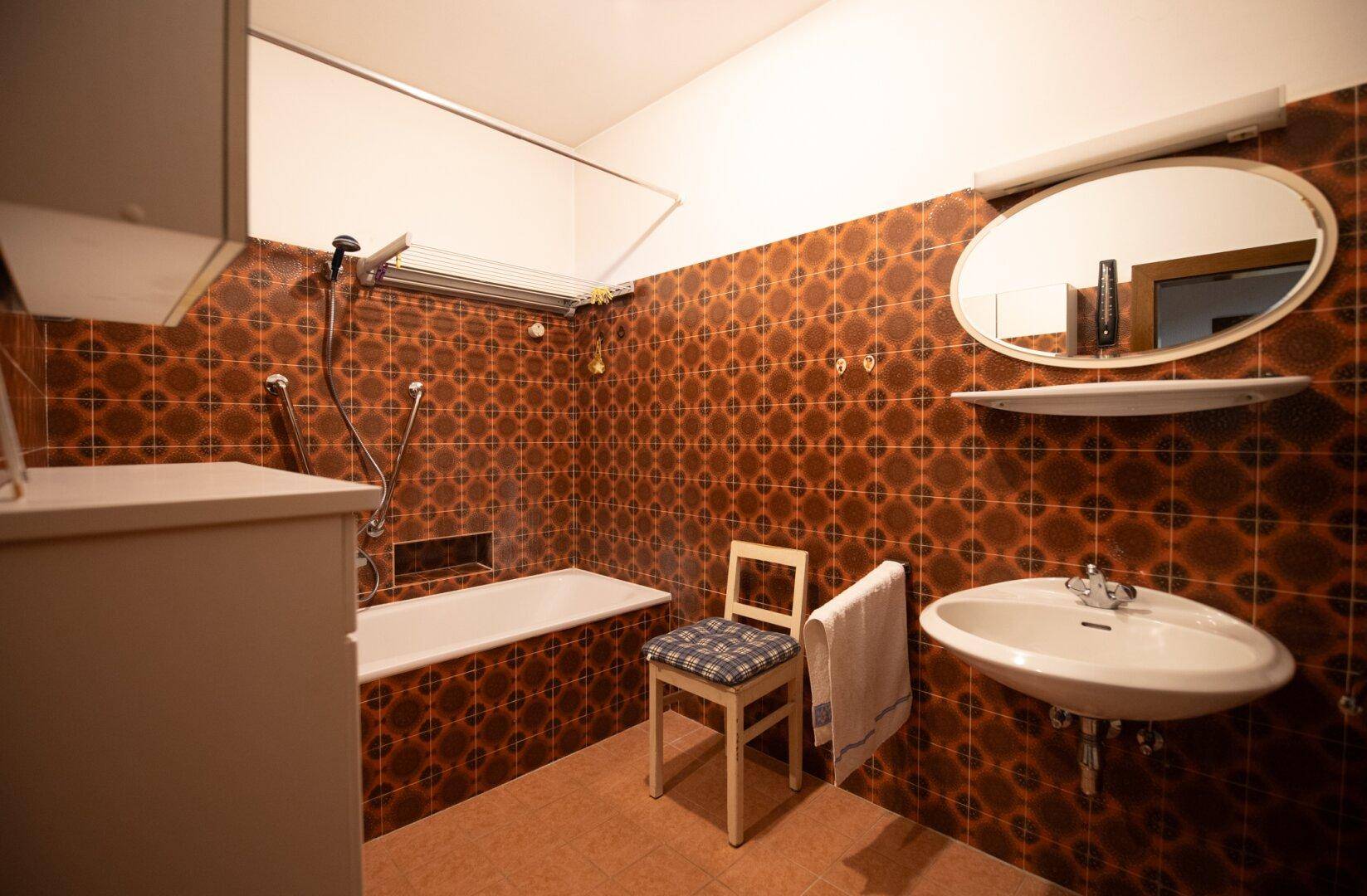 Badezimmer im 80er-Jahre-Stil mit braunen Fliesen und Badewanne, funktional und gut erhalten.