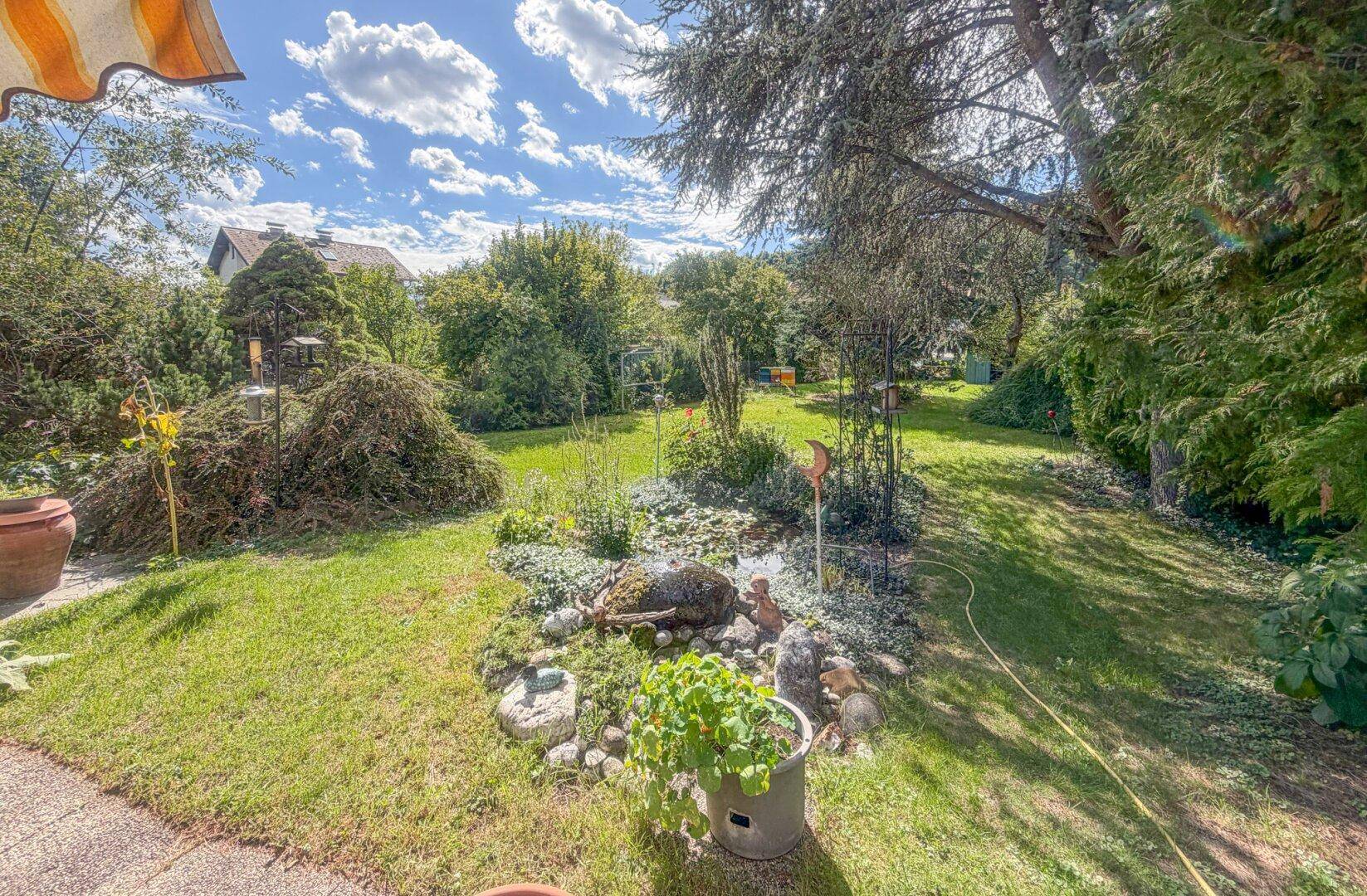 Weitläufiger Garten mit üppiger Vegetation, Rasen und schattenspendenden Bäumen, ideal zur Entspannung.