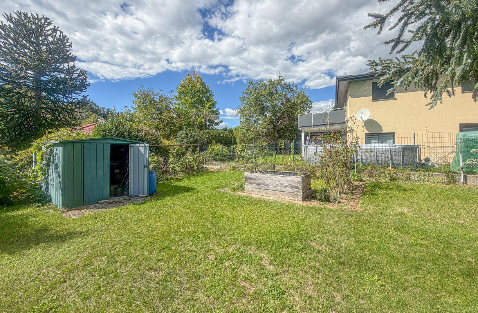 Hinterer Gartenbereich mit Geräteschuppen, Hochbeet und viel Grünfläche, ideal für Gartenliebhaber.