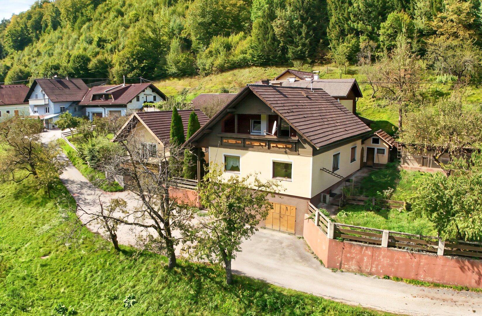 Traditionelles Haus mit braunem Ziegeldach und Balkon in grüner, hügeliger Umgebung.