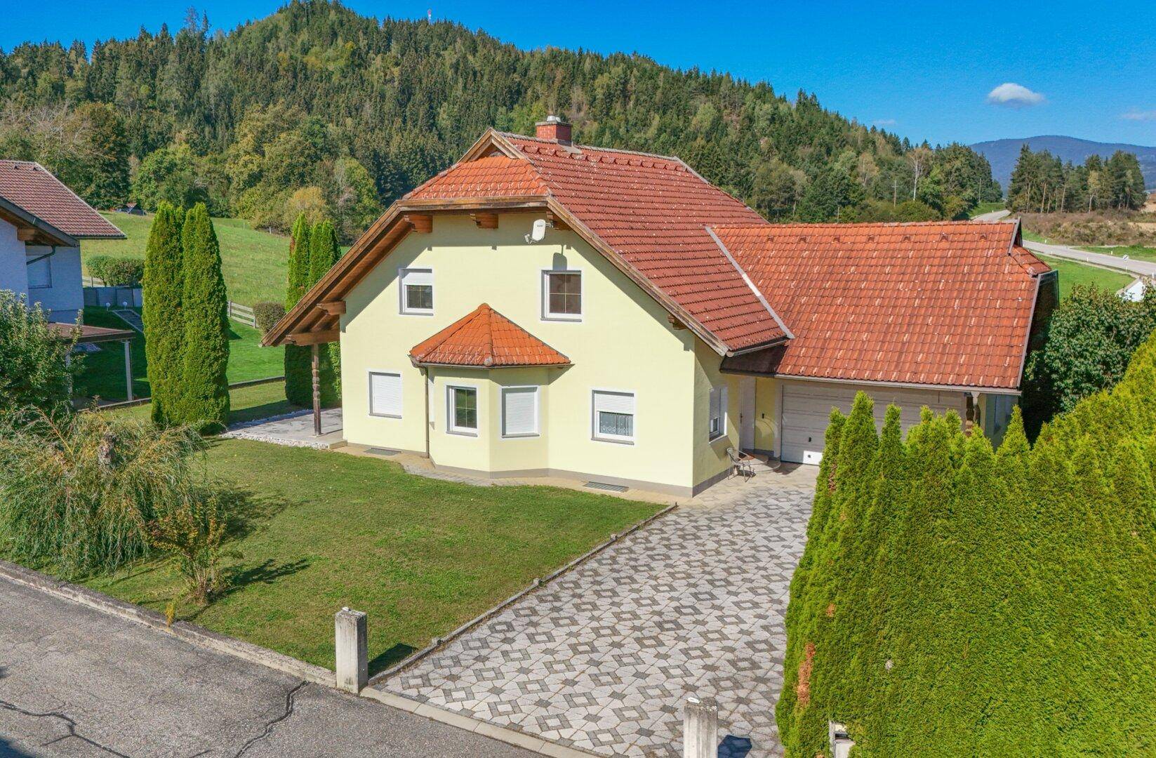 Wohnhaus in ländlicher Umgebung mit großer Auffahrt, umgeben von Bäumen und Hecken.