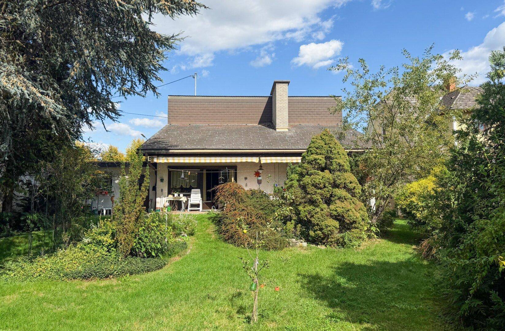 Weitläufiger Gartenbereich mit Terrasse und Blick auf die Rückseite des Einfamilienhauses.
