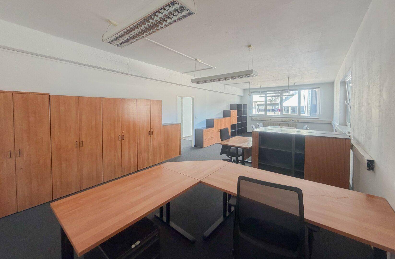 Geräumiges Büro mit mehreren Schreibtischen, Holzschränken und Teppichboden.