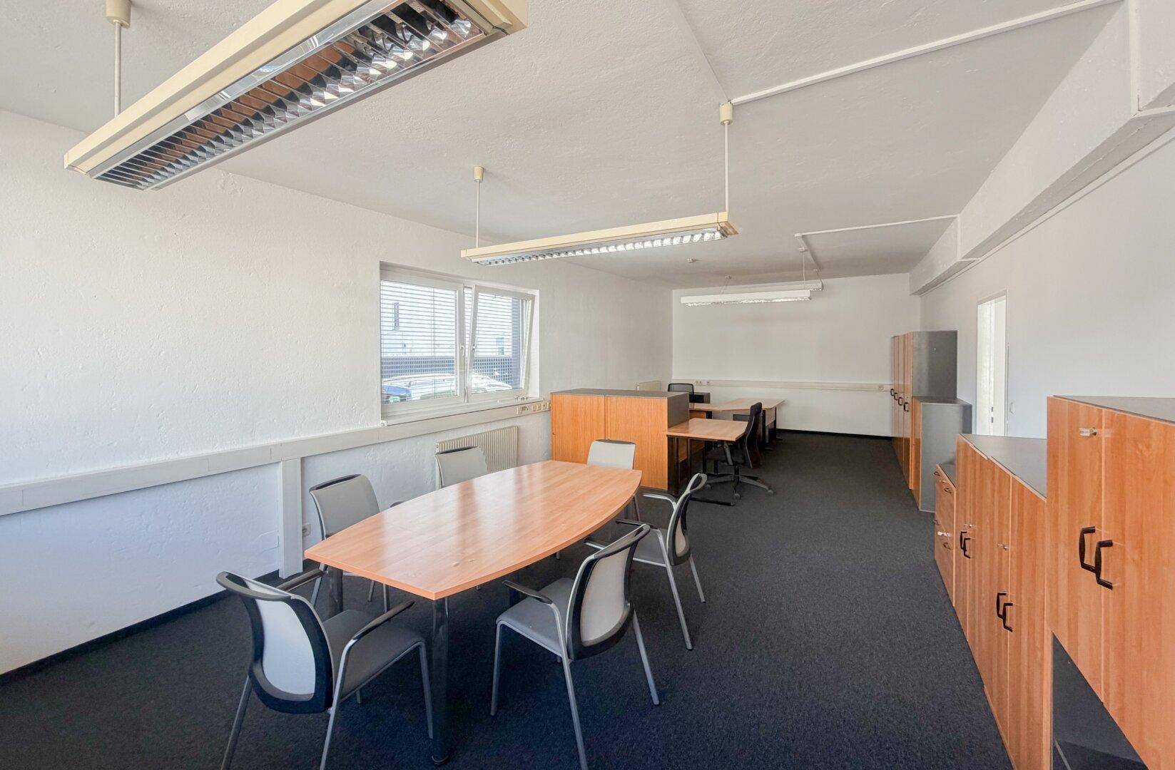 Konferenzbereich in einem Büro mit ovalem Tisch, Stühlen und Holzschränken.