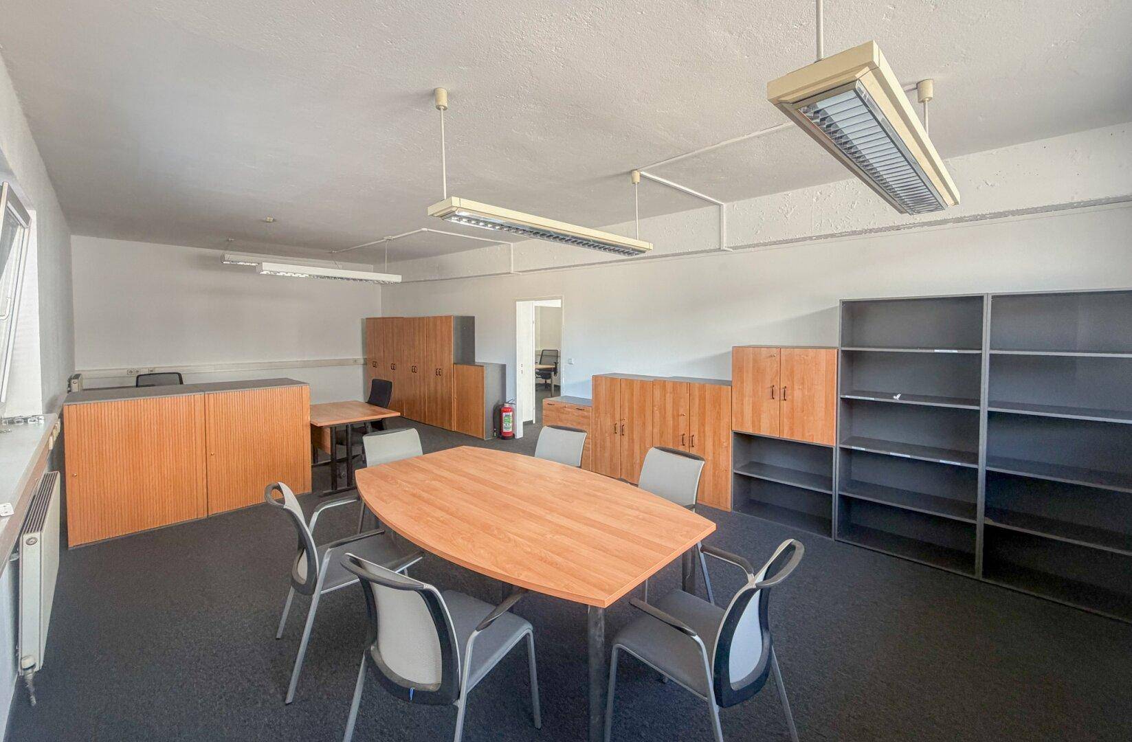 Großes Büro mit verschiedenen Arbeitsbereichen, Konferenztisch und Regalen.