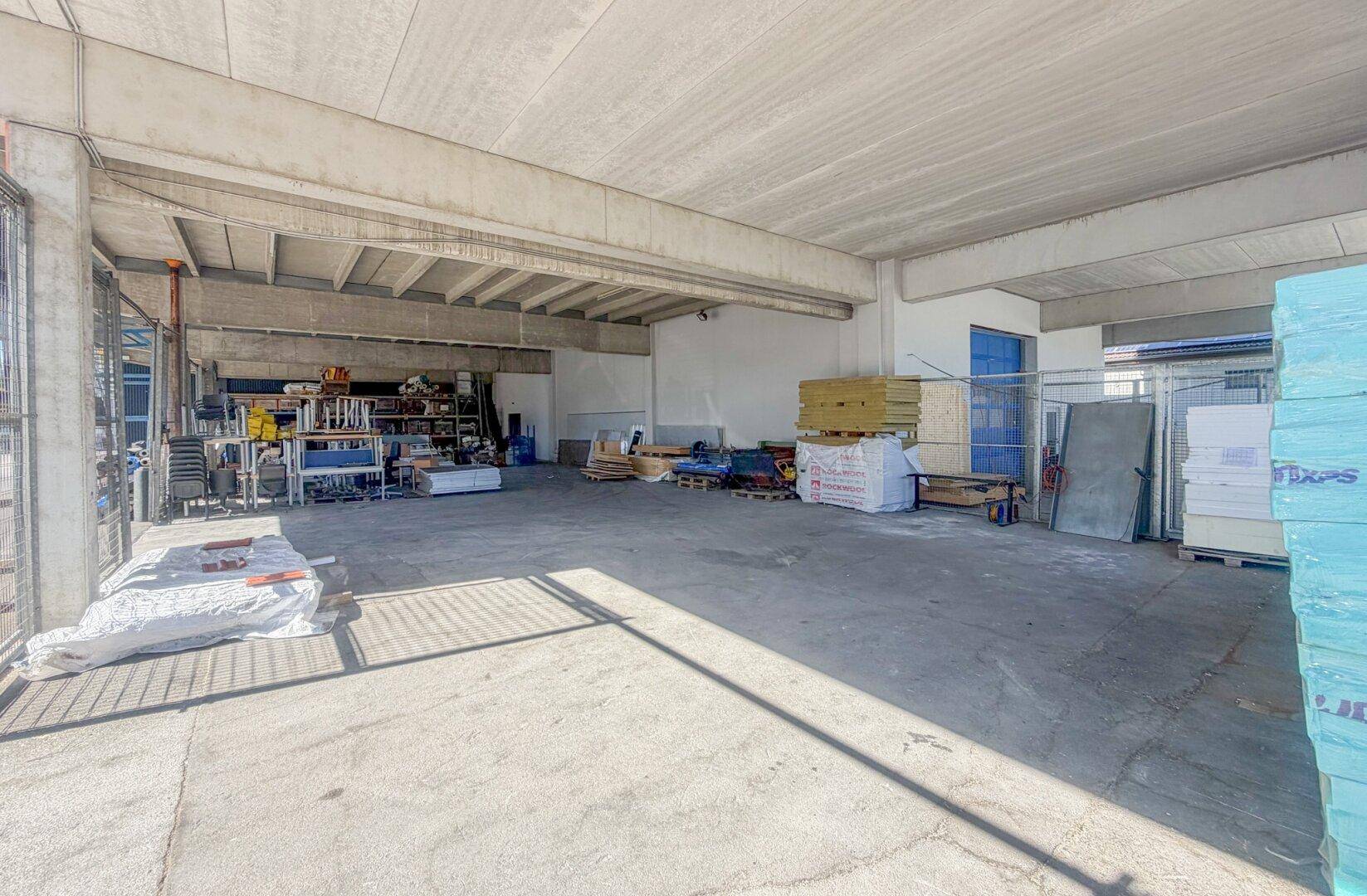 Geräumige Lagerhalle mit Betonboden, hohen Decken und verschiedenen Materialien.
